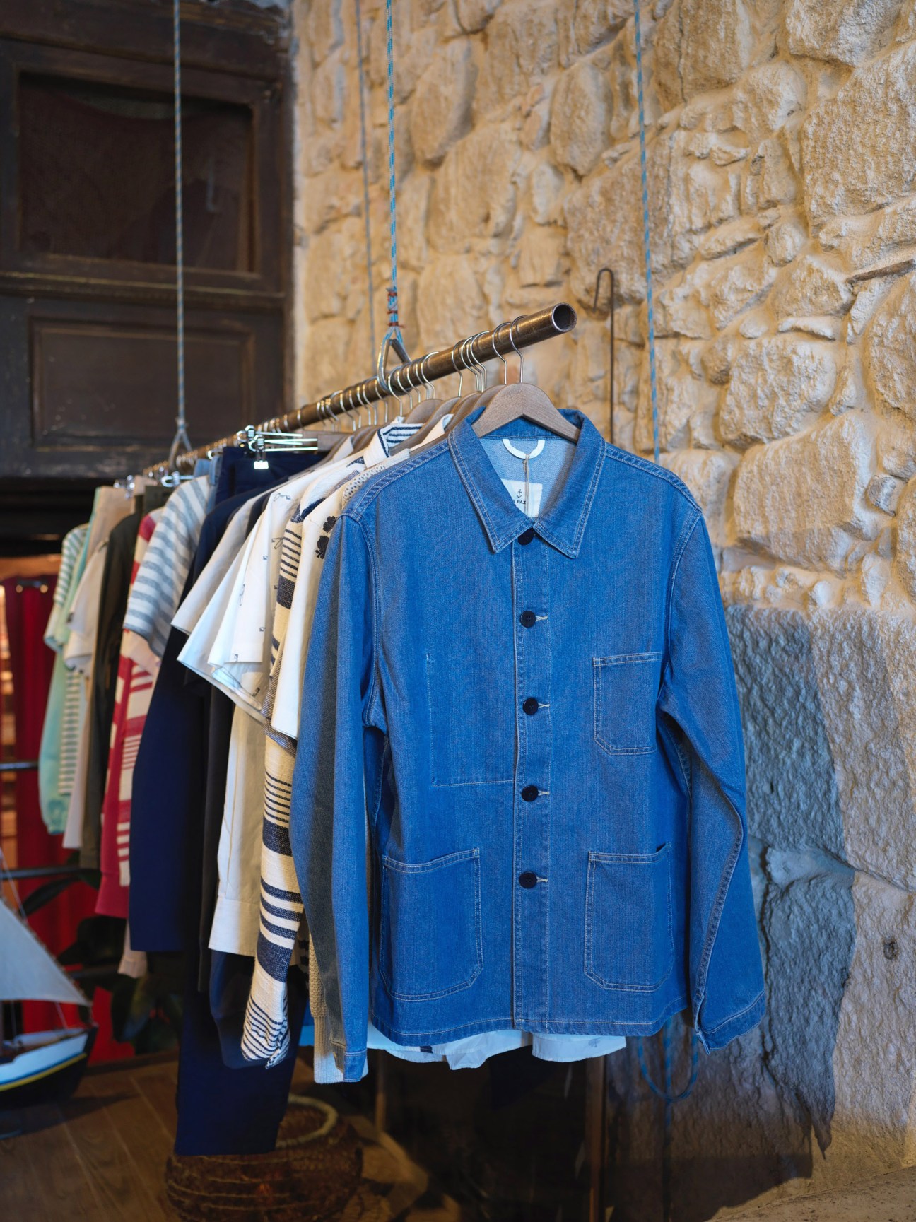 Blue denim shirt on hanger displayed alongside other La Paz clothing items against stone wall.
