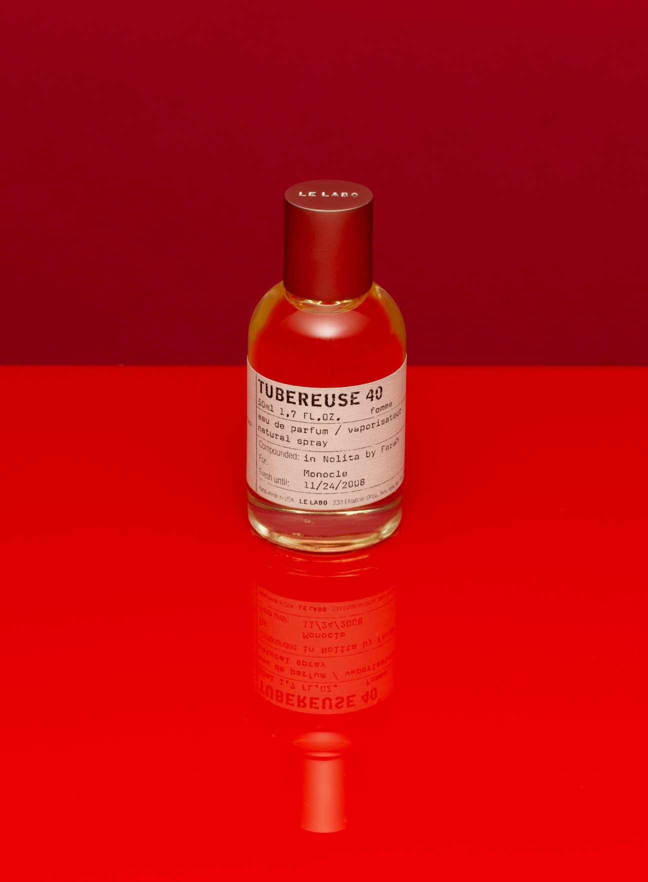 Le Labo Tubereuse 40 perfume bottle with red cap on red background.