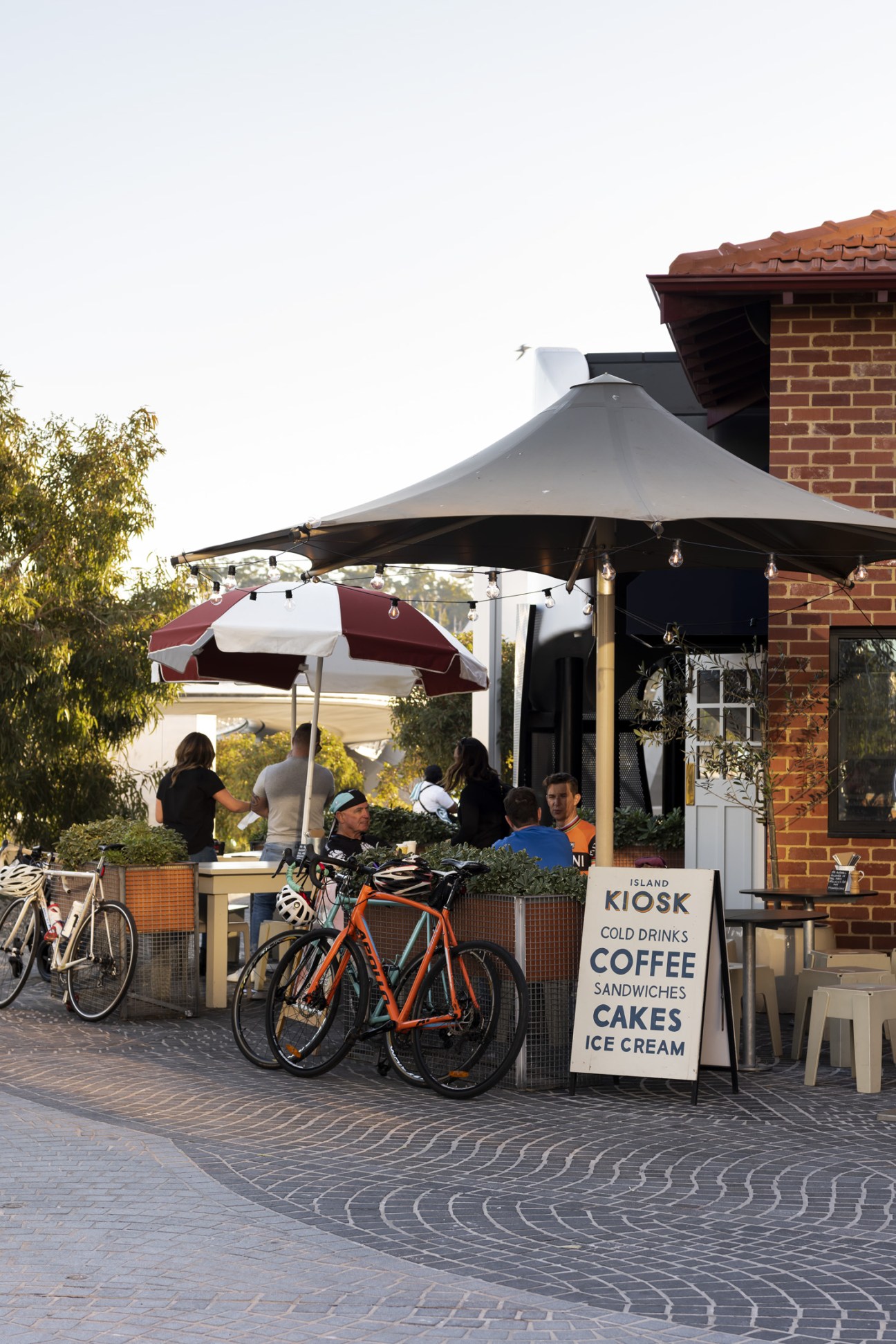 The Island Kiosk at Elizabeth Quay with outdoor seating under umbrellas, bicycles parked nearby, and brick heritage building.