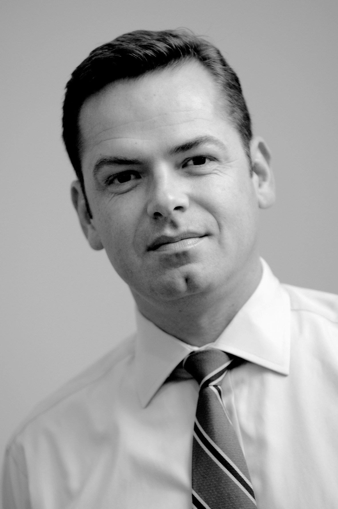 Black and white portrait of Peter Reid wearing a white shirt and striped tie.