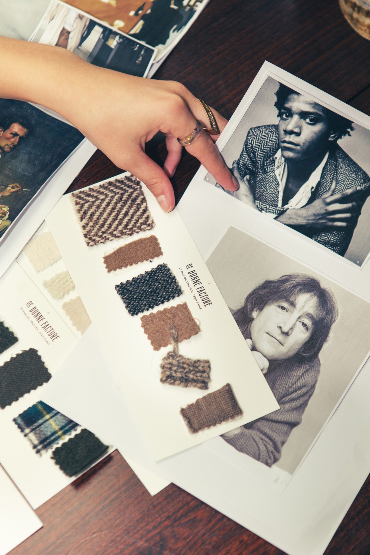 Hand pointing at fabric swatches and black and white portrait photographs spread on wooden surface