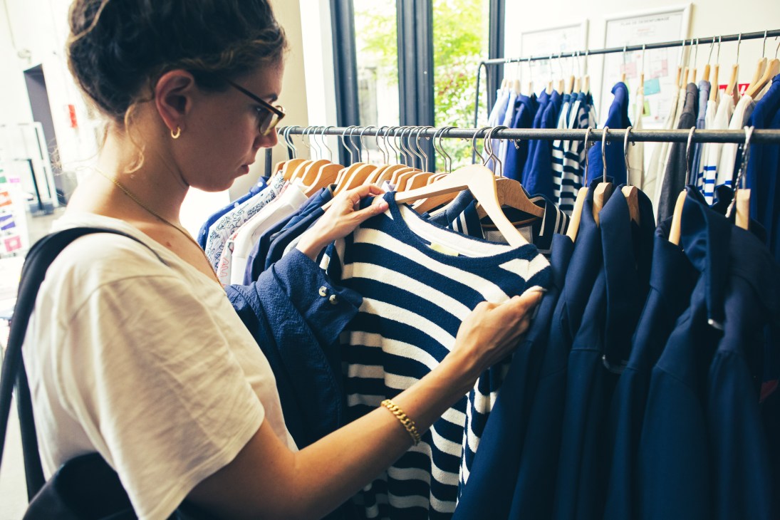 Woman with glasses examining striped clothing on hangers in a retail setting