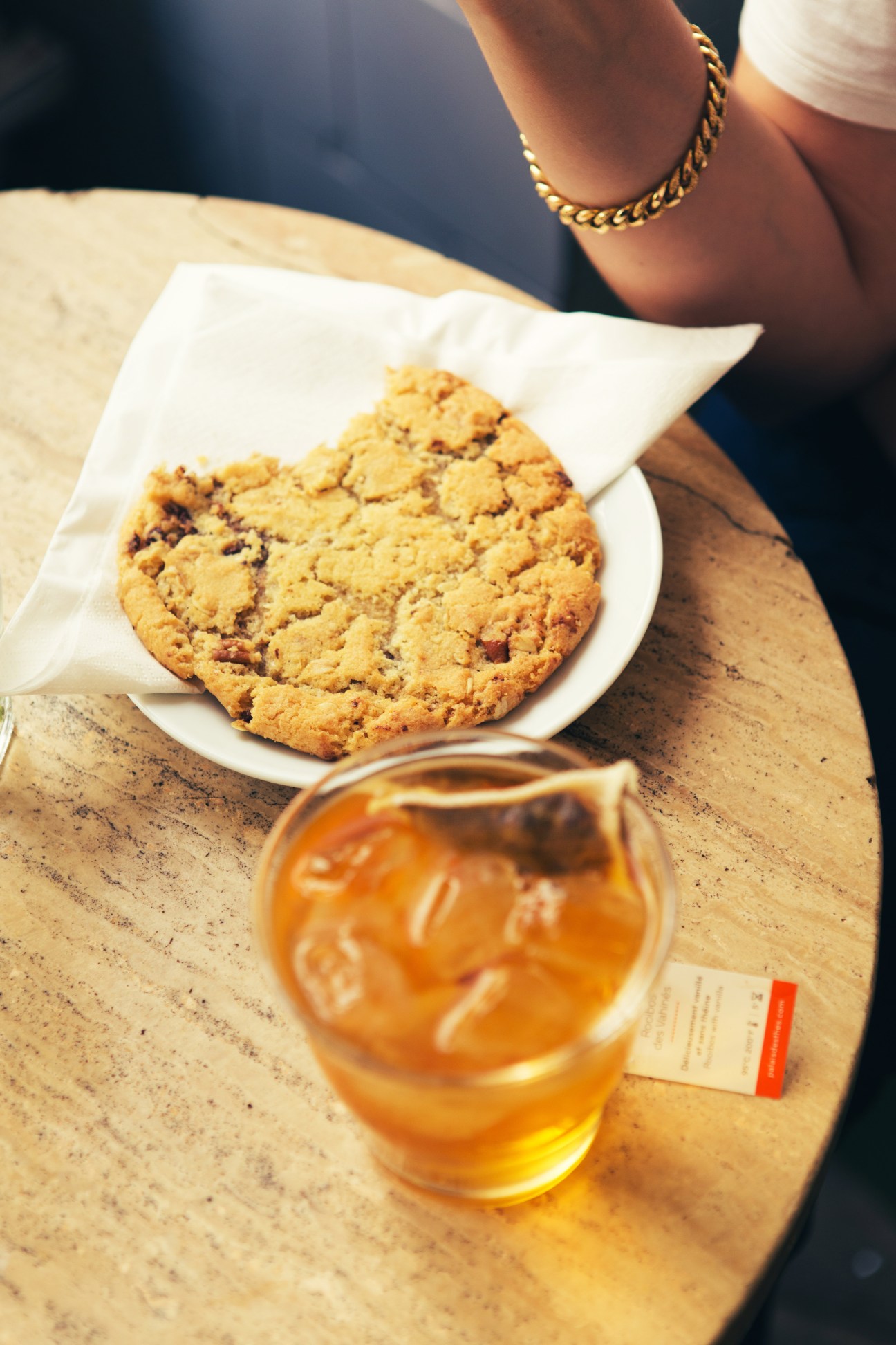 A chocolate chip cookie on a white napkin and a glass of tea on a wooden table at Boot Café