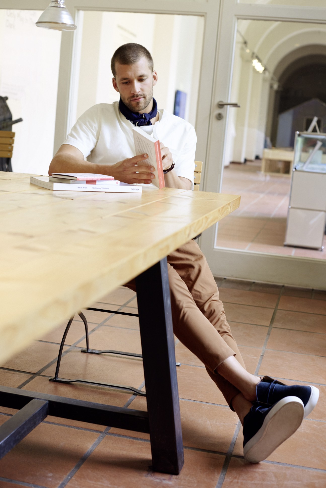 Man in casual outfit reading at wooden table in bright interior space.