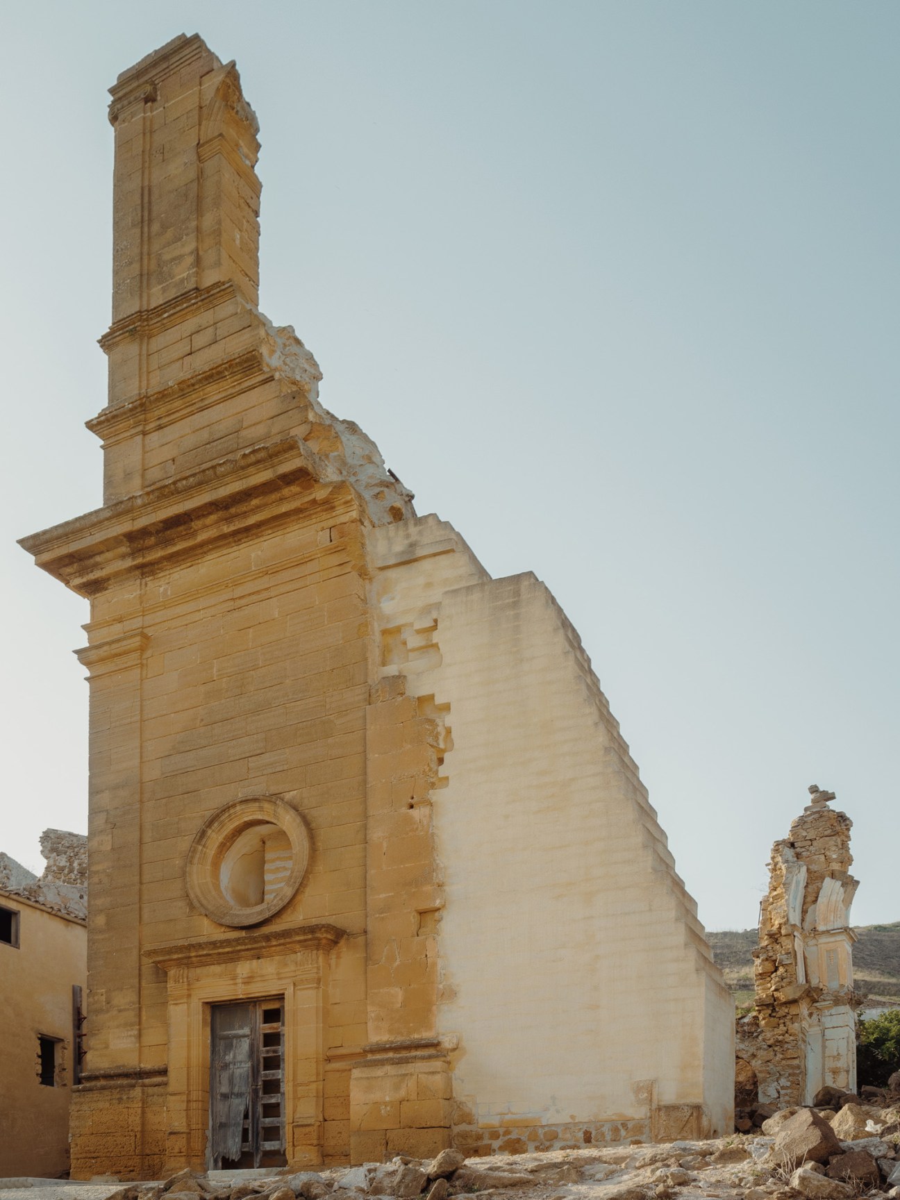 Deteriorating stone church tower with rounded window and cupola in ruins of Poggioreale