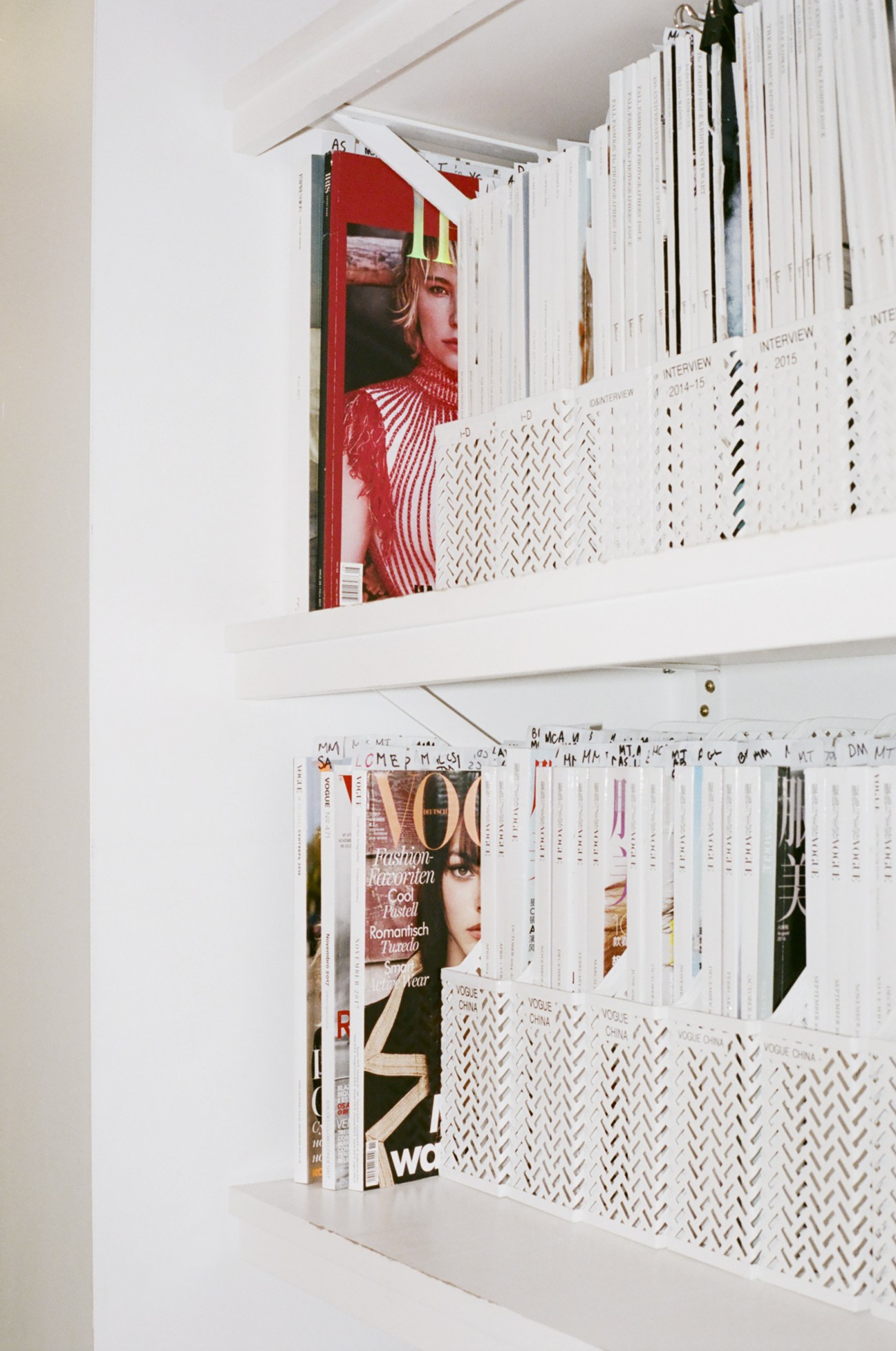 White shelving unit displaying stacked fashion magazines and publications with visible cover photography.
