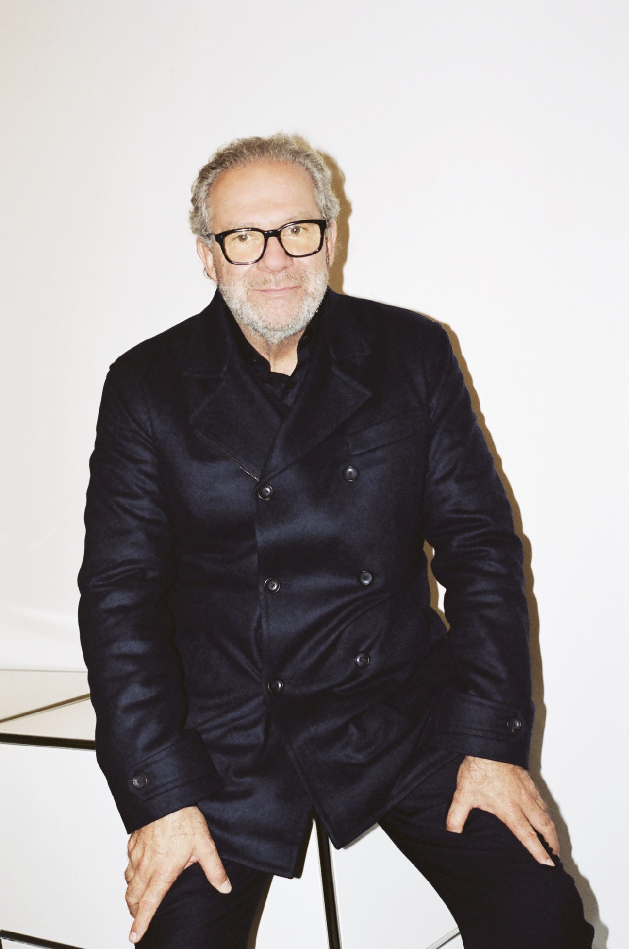 Giovanni Testino wearing glasses and a dark double-breasted blazer seated against a white background