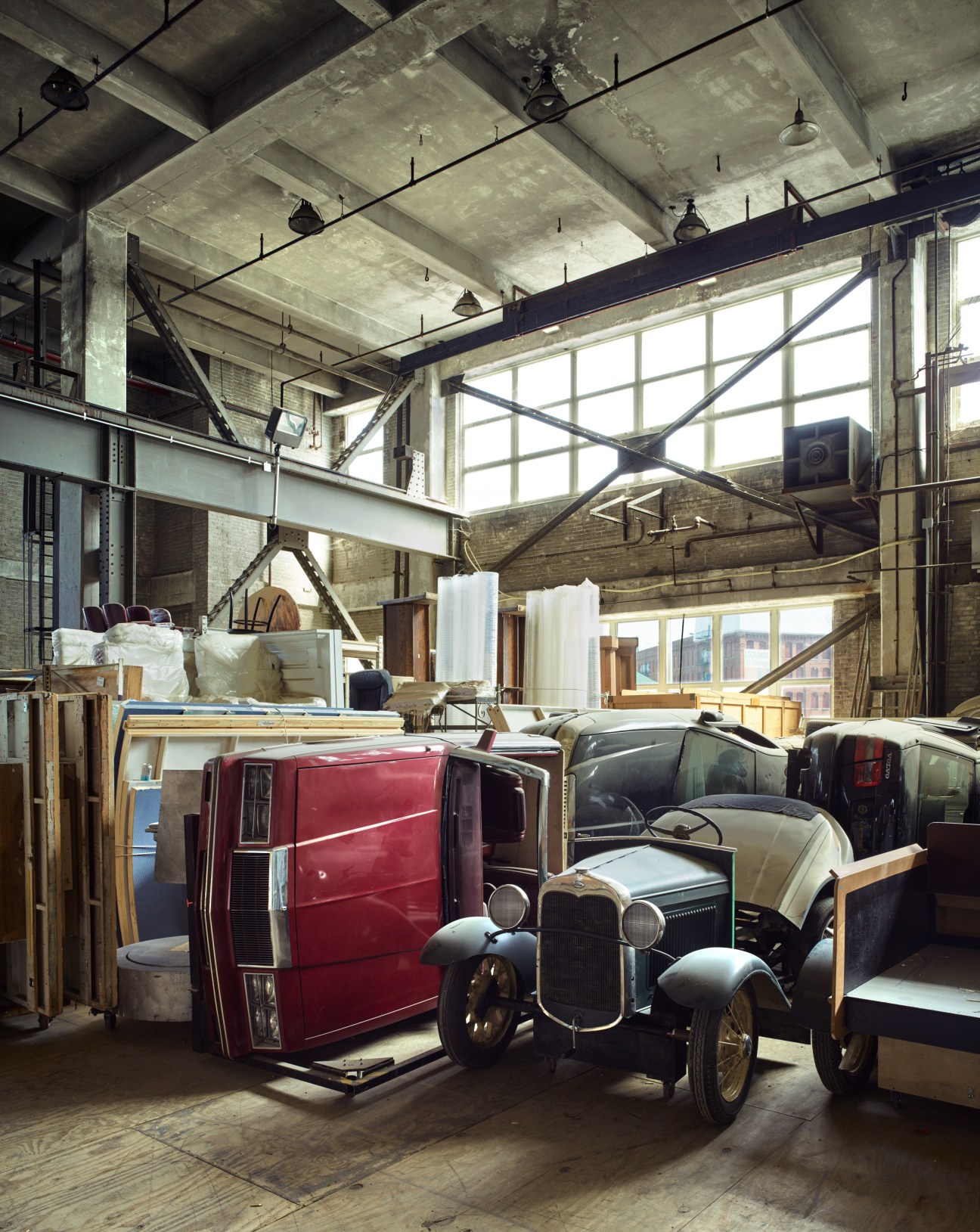 Vintage prop cars stored in an industrial warehouse with high ceilings and large windows.