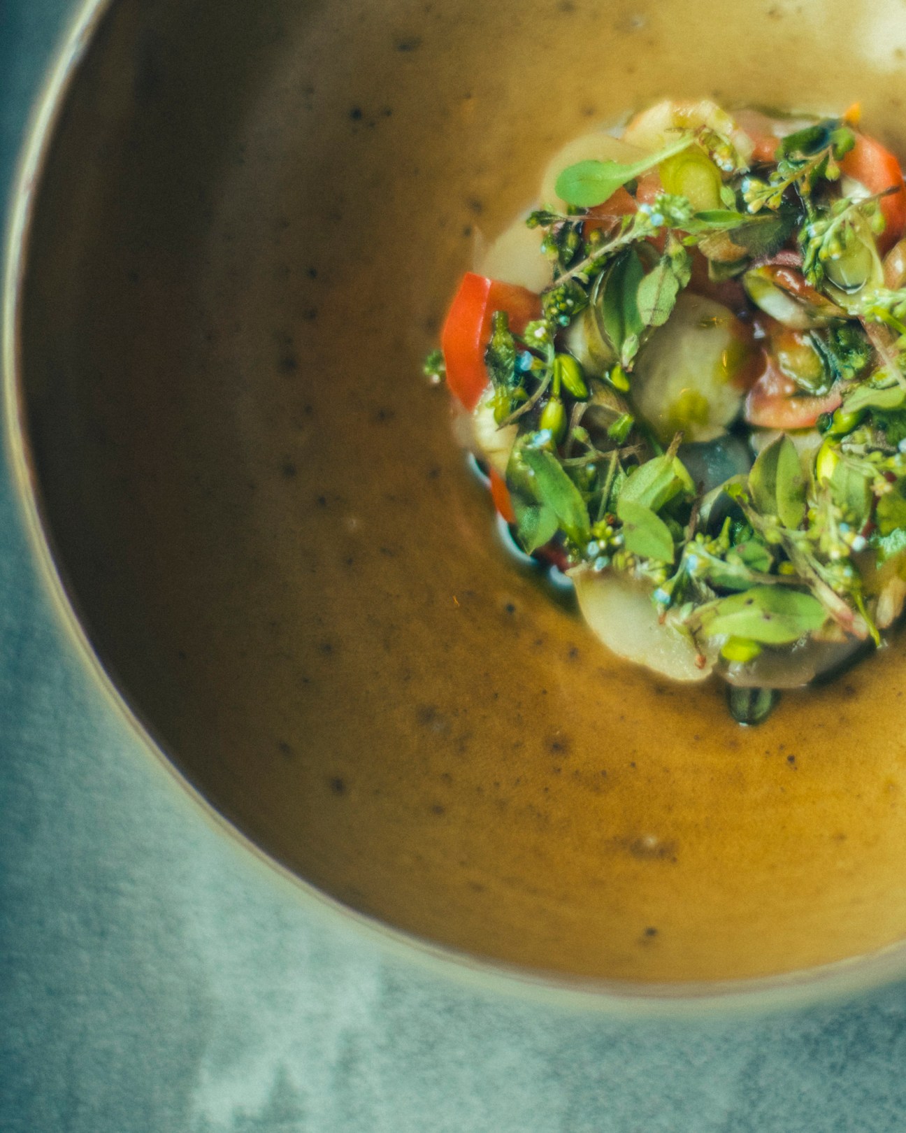A bowl of golden broth soup garnished with fresh green herbs and colorful vegetables in an artistic presentation