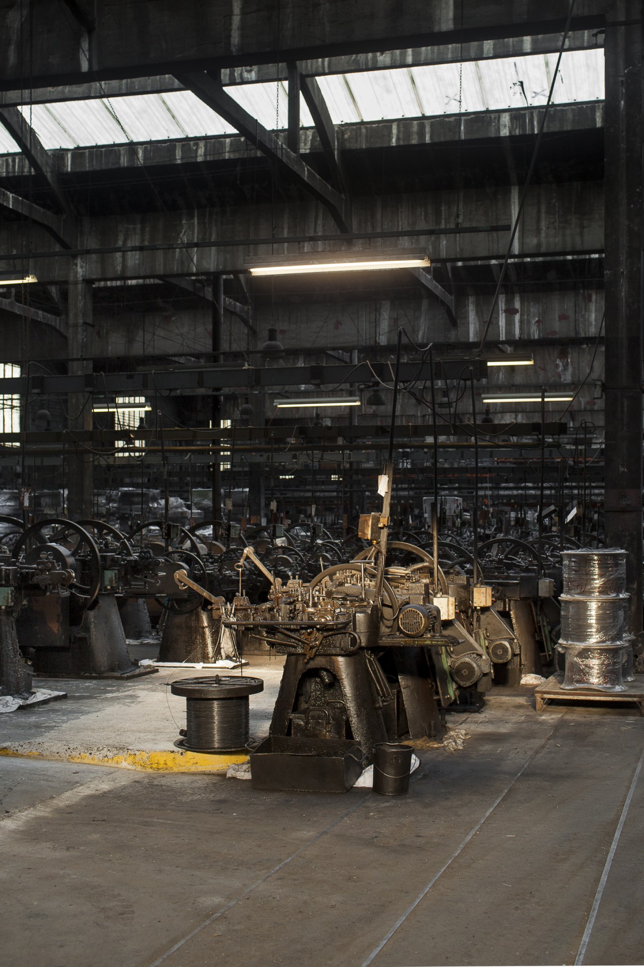 A century-old nail-making machine operates in Rivierre factory's industrial warehouse setting.