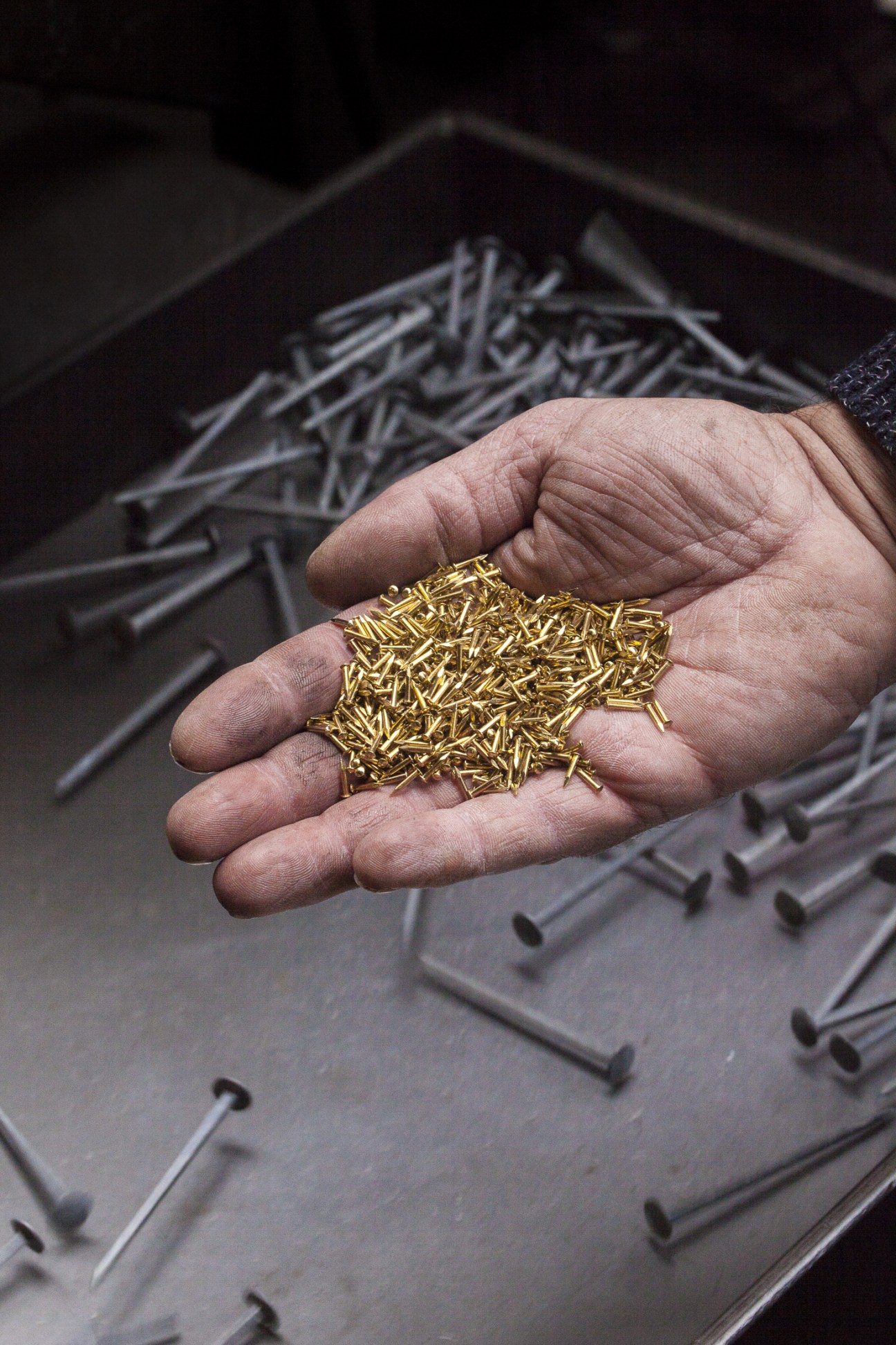 Hand holding small gold-finished nails produced at Rivierre factory.