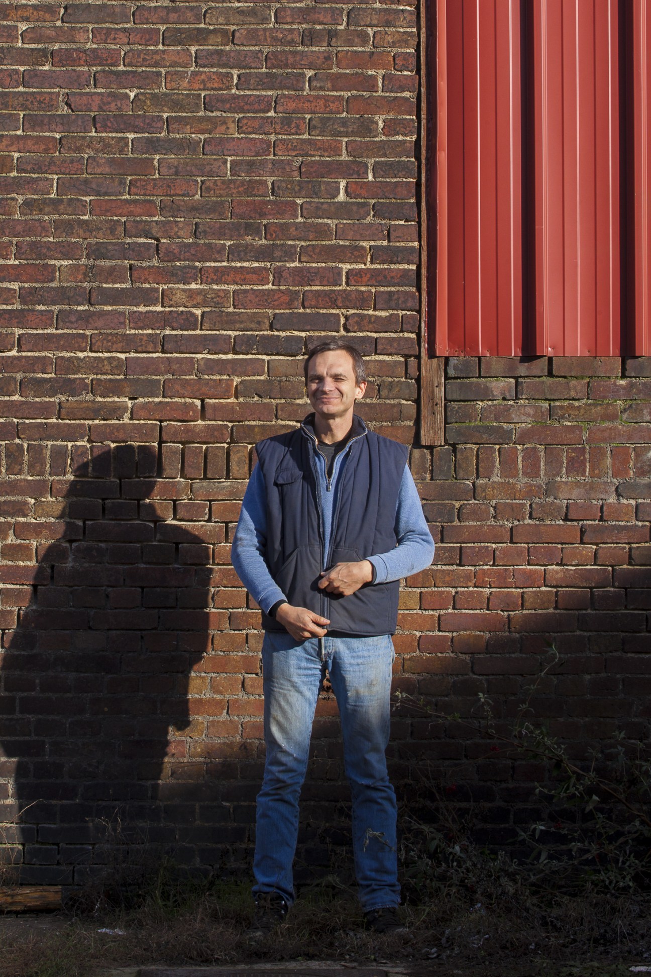 Luc Kemp, owner of Rivierre nail factory, standing against a brick wall wearing a navy vest and blue shirt.