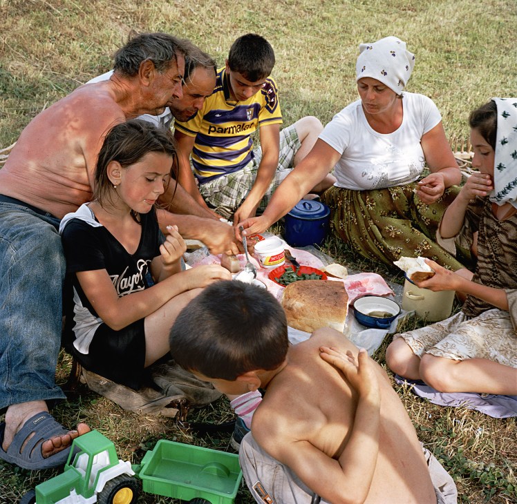 A Romanian family gathered outdoors sharing food and relaxation after a day of work in Maramures.