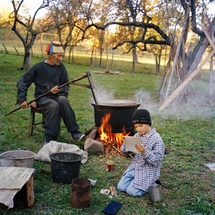 A man and boy cook plum jam over a fire in an orchard in Transylvania, Romania.