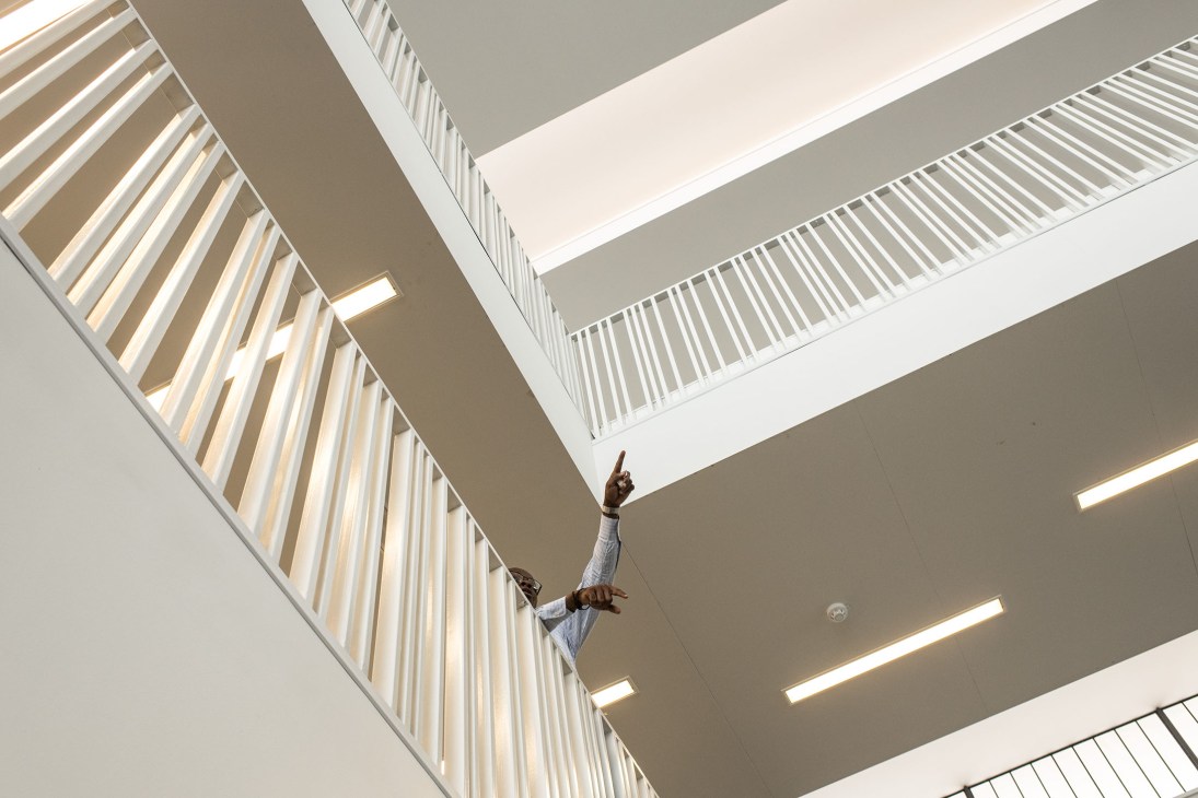 Person viewed from below making a peace sign while standing on an interior staircase with modern white railings.