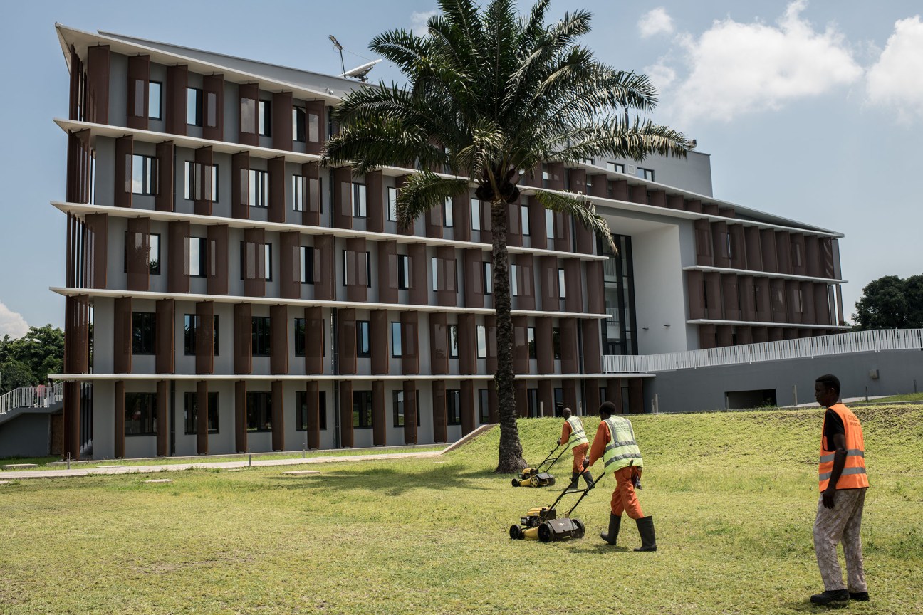 Congolese workers in safety vests mowing the lawn at the new Belgian embassy in Kinshasa.