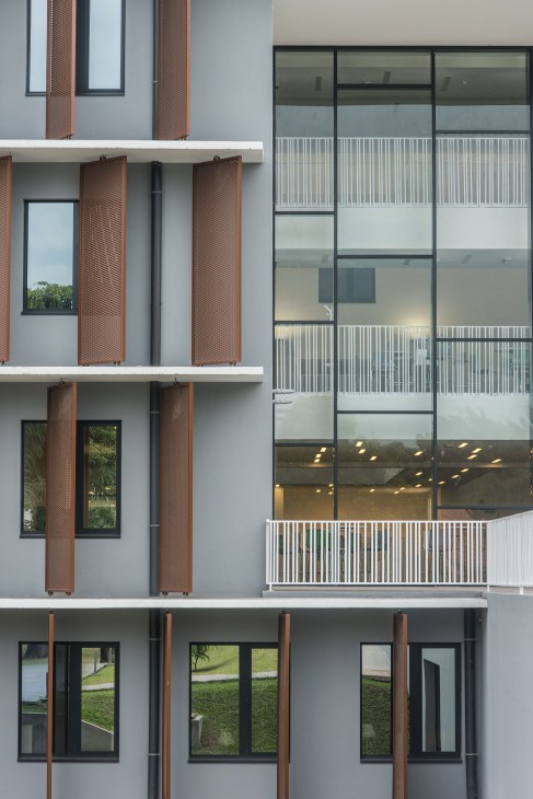 Modern multi-story building facade with brick pillars, white panels, and floor-to-ceiling windows with metal railings.