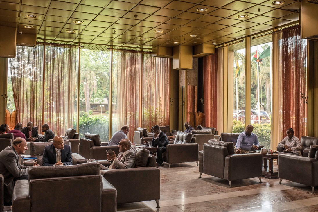 Business people conduct meetings in the modern lobby of the Rainbow Towers Hotel in Harare, with floor-to-ceiling windows overlooking the grounds.