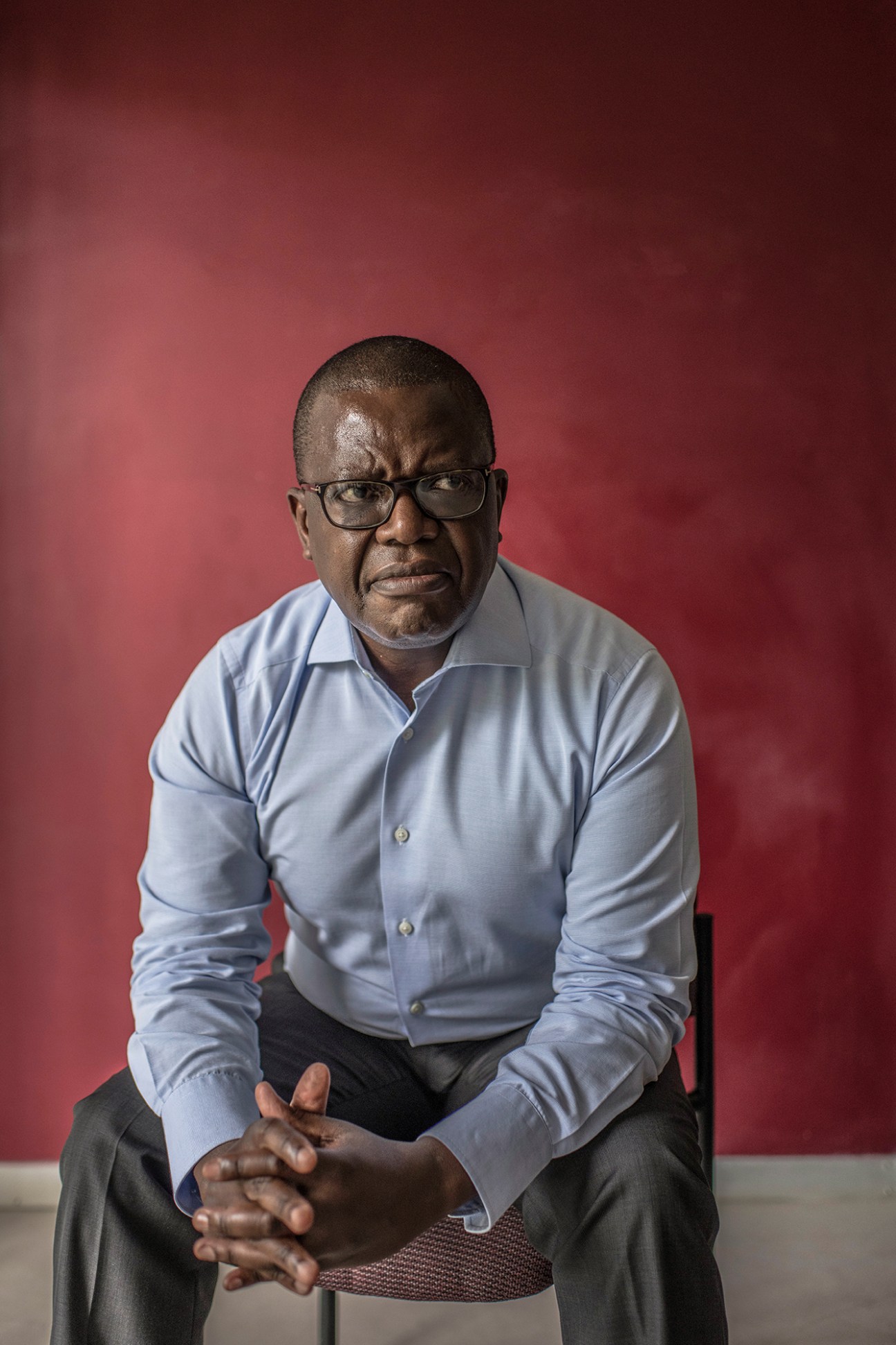 Trevor Ncube, owner of Zimbabwe's three main independent newspapers, sits against a red background wearing a light blue shirt.