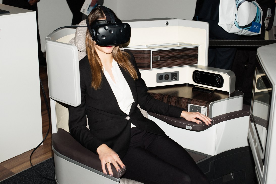 Woman wearing HTC Vive headset seated in Recaro aircraft cabin mockup with controls and displays.