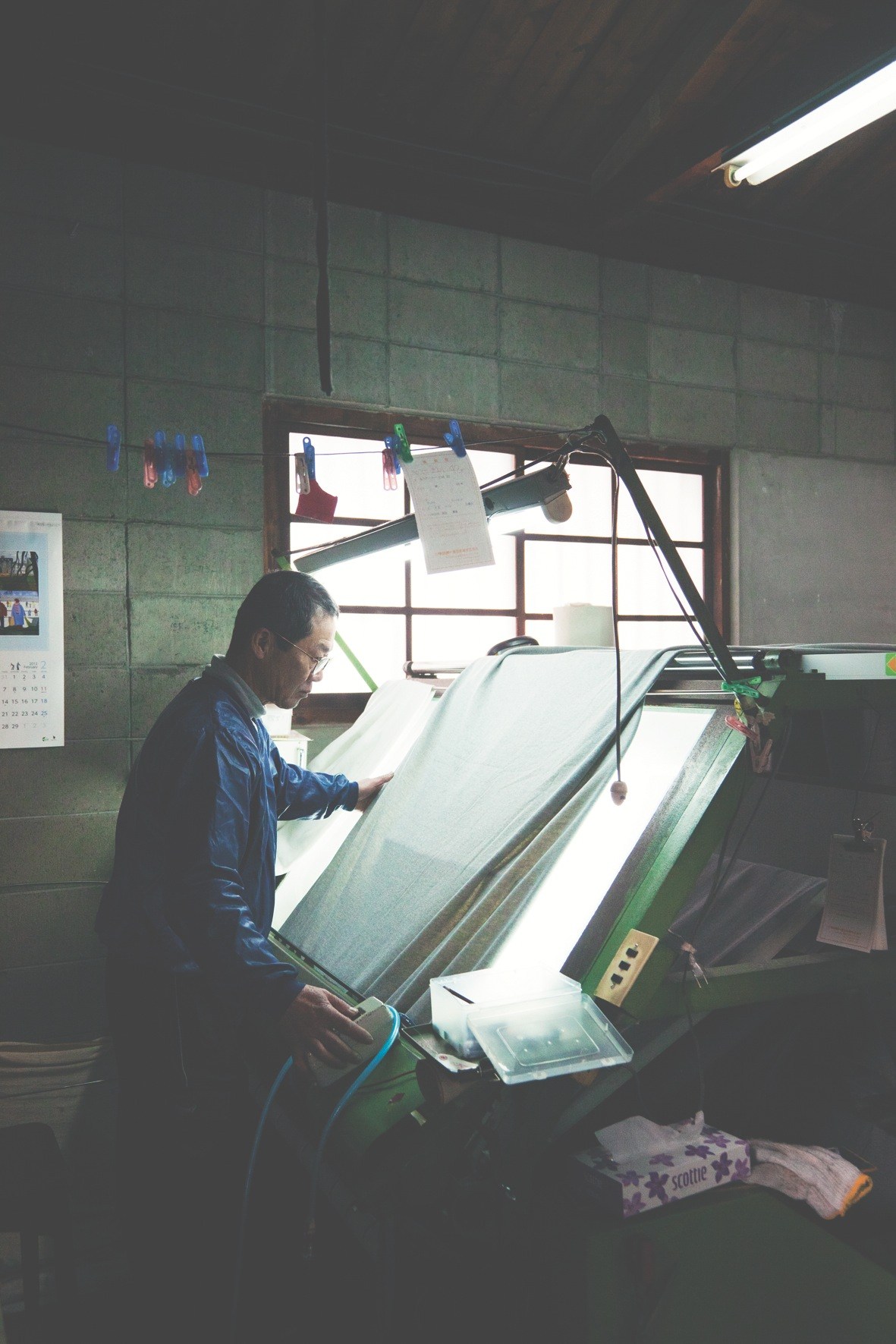 Factory worker inspects newly knitted cloth for quality at Kanekichi Industries.