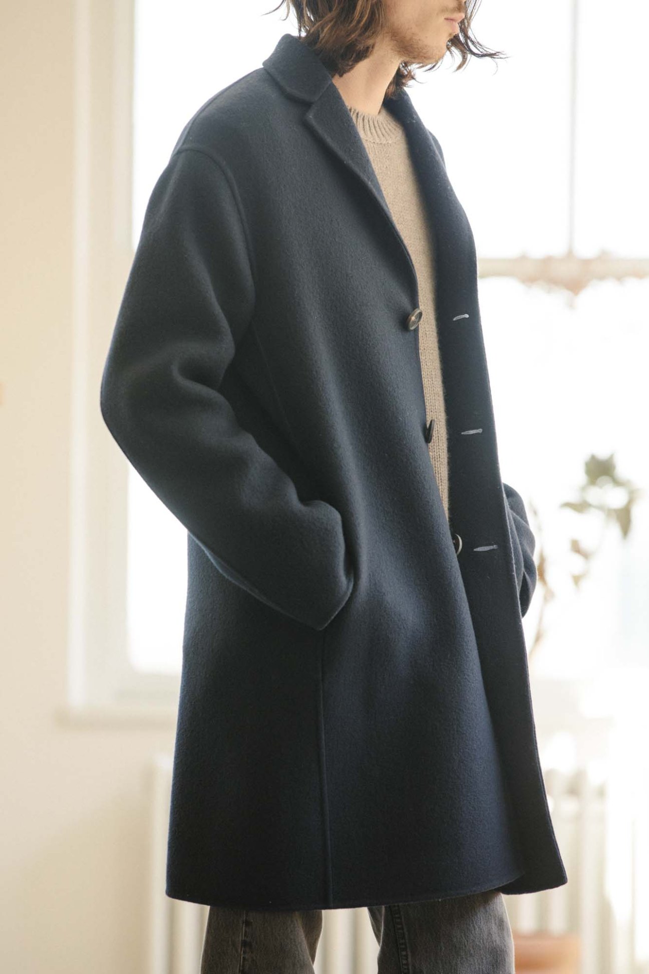 Model wearing navy cashmere coat and cream crewneck sweater against neutral background
