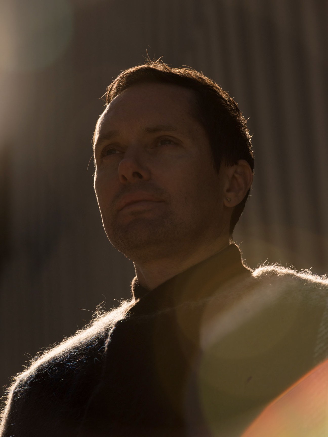 Portrait of Mike Milosh from Rhye in warm backlighting against a neutral background.