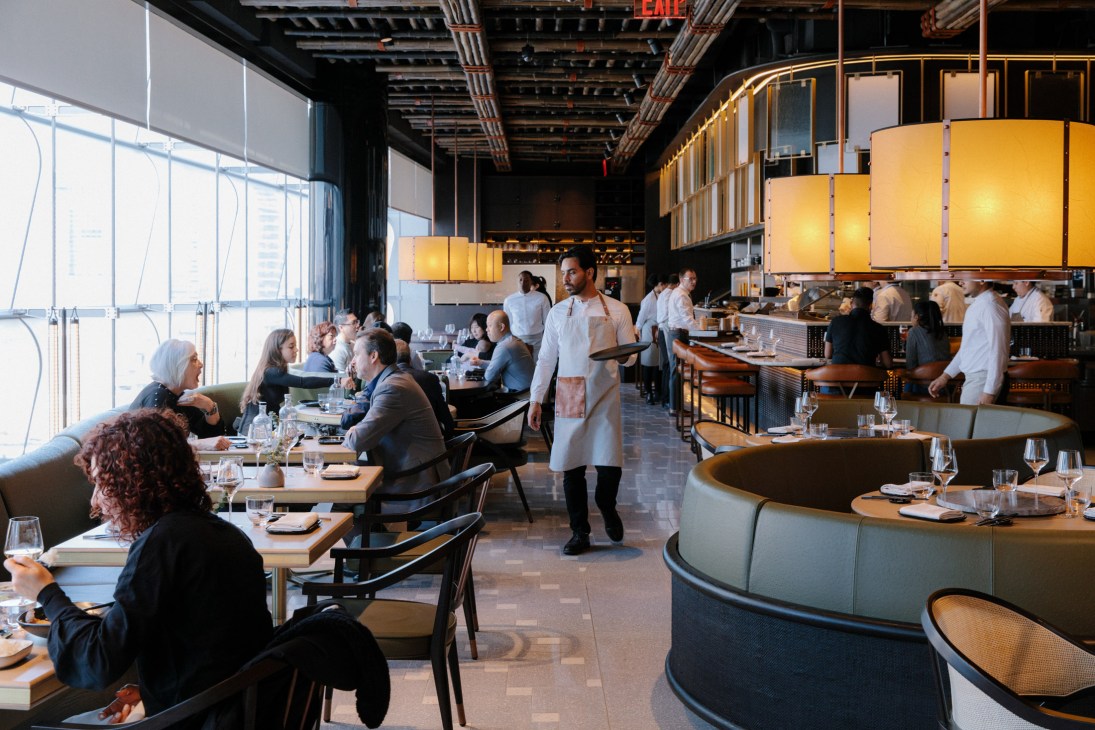 Diners seated at tables during lunch service at Wild Ink restaurant with floor-to-ceiling windows and yellow pendant lighting.