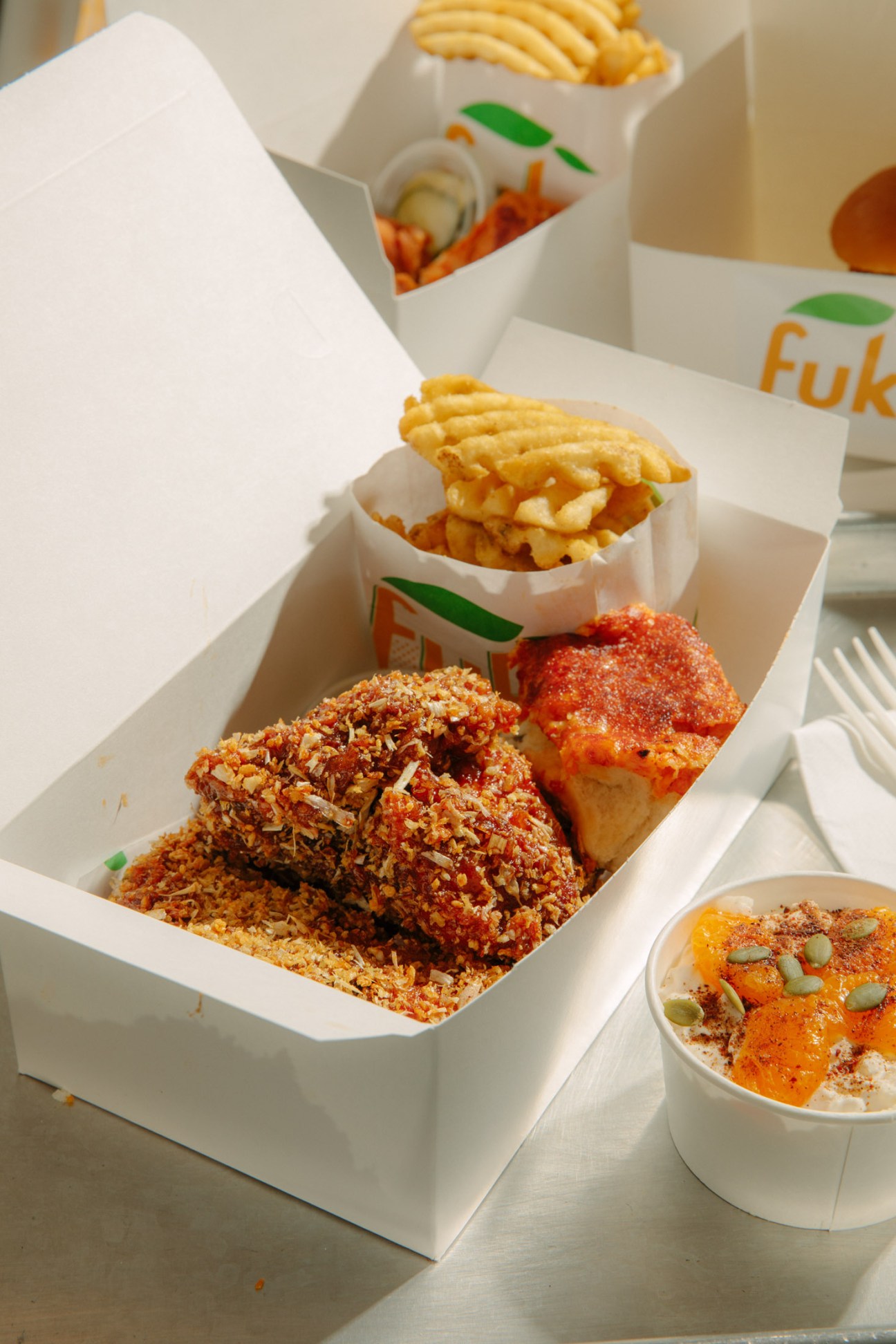 Fried chicken and waffle fries in branded takeout containers from Momofuku Fuku.