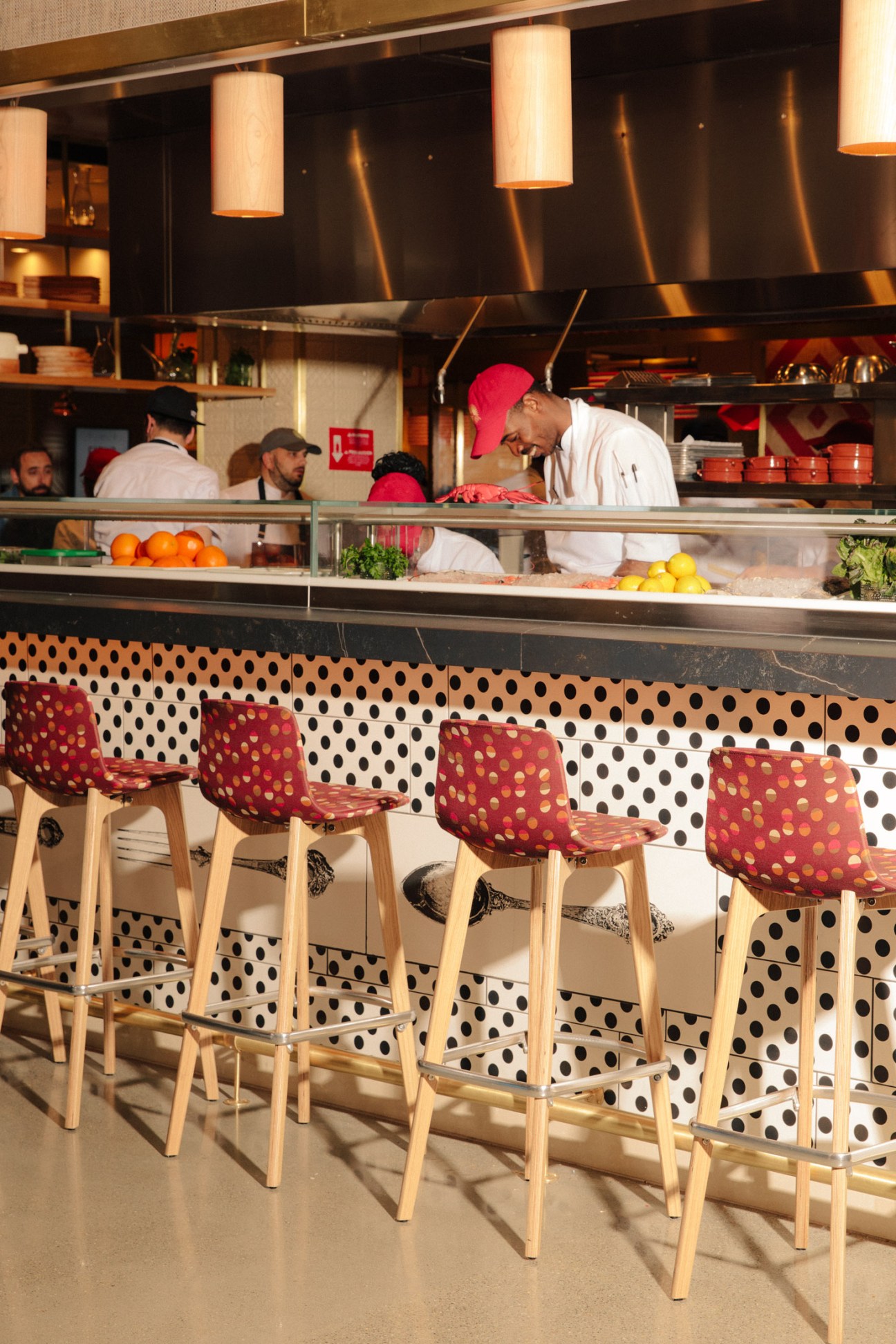 Chef preparing food at counter in Mercado Little Spain with bar seating and polka-dot backdrop.