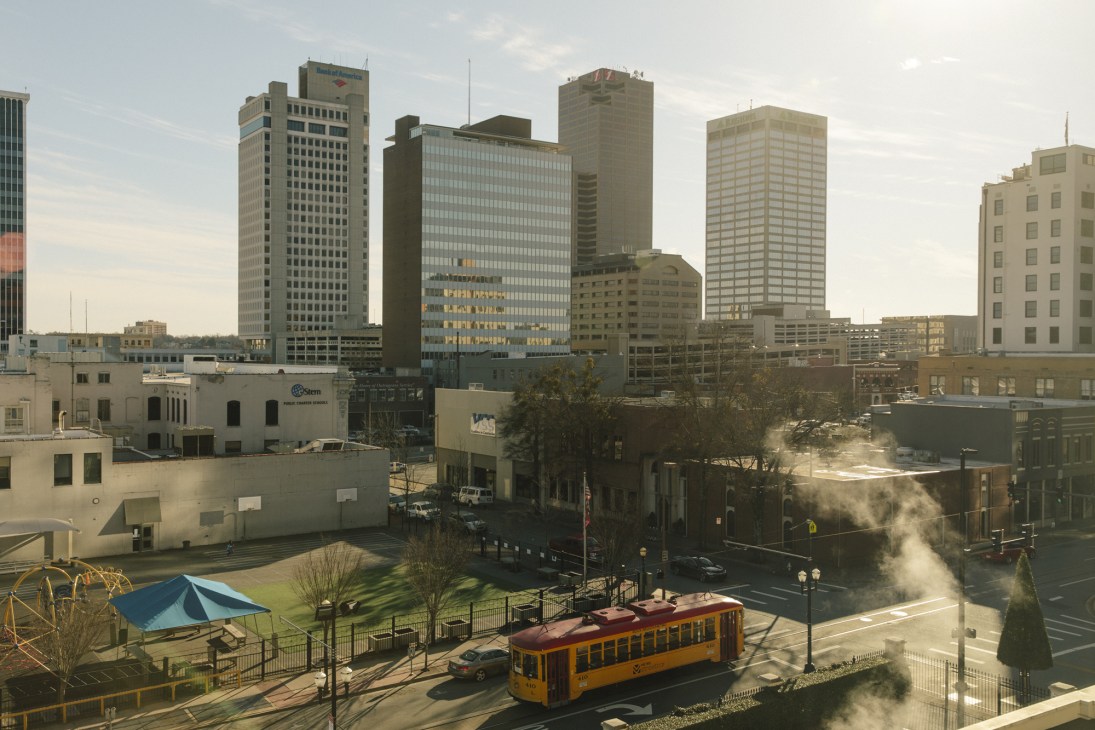 Yellow streetcar traveling through downtown Little Rock with high-rise buildings and street-level development in background.