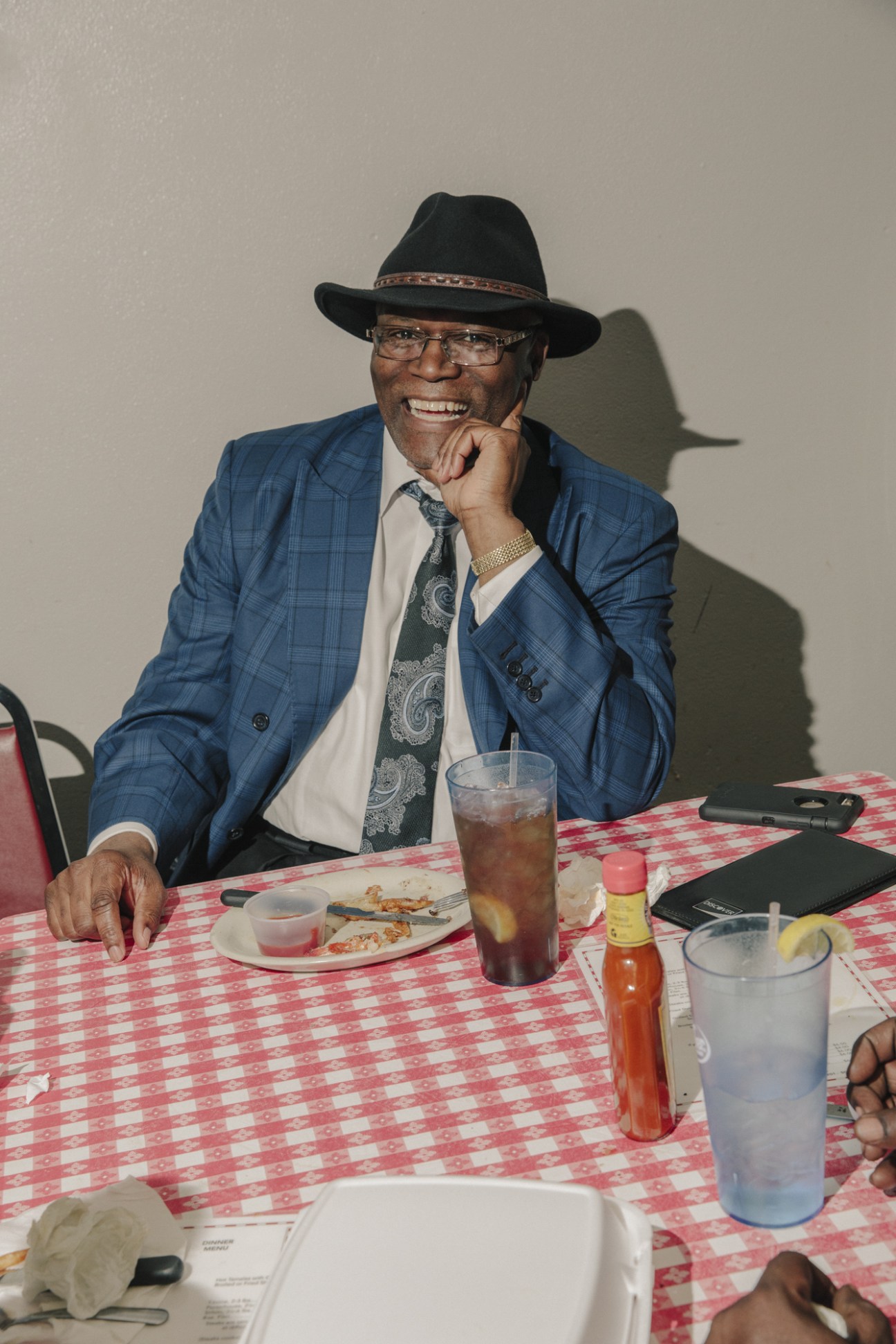 Robert Robinson seated at a table at Doe's Eat Place, wearing a blue plaid blazer and black hat.