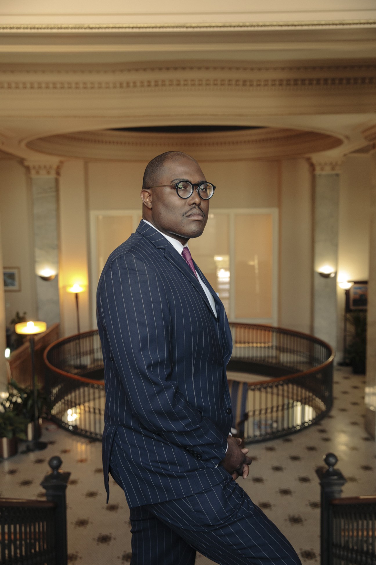 Frank Scott Jr, mayor of Little Rock, wearing a navy pinstriped suit and glasses in an ornate historic building interior.
