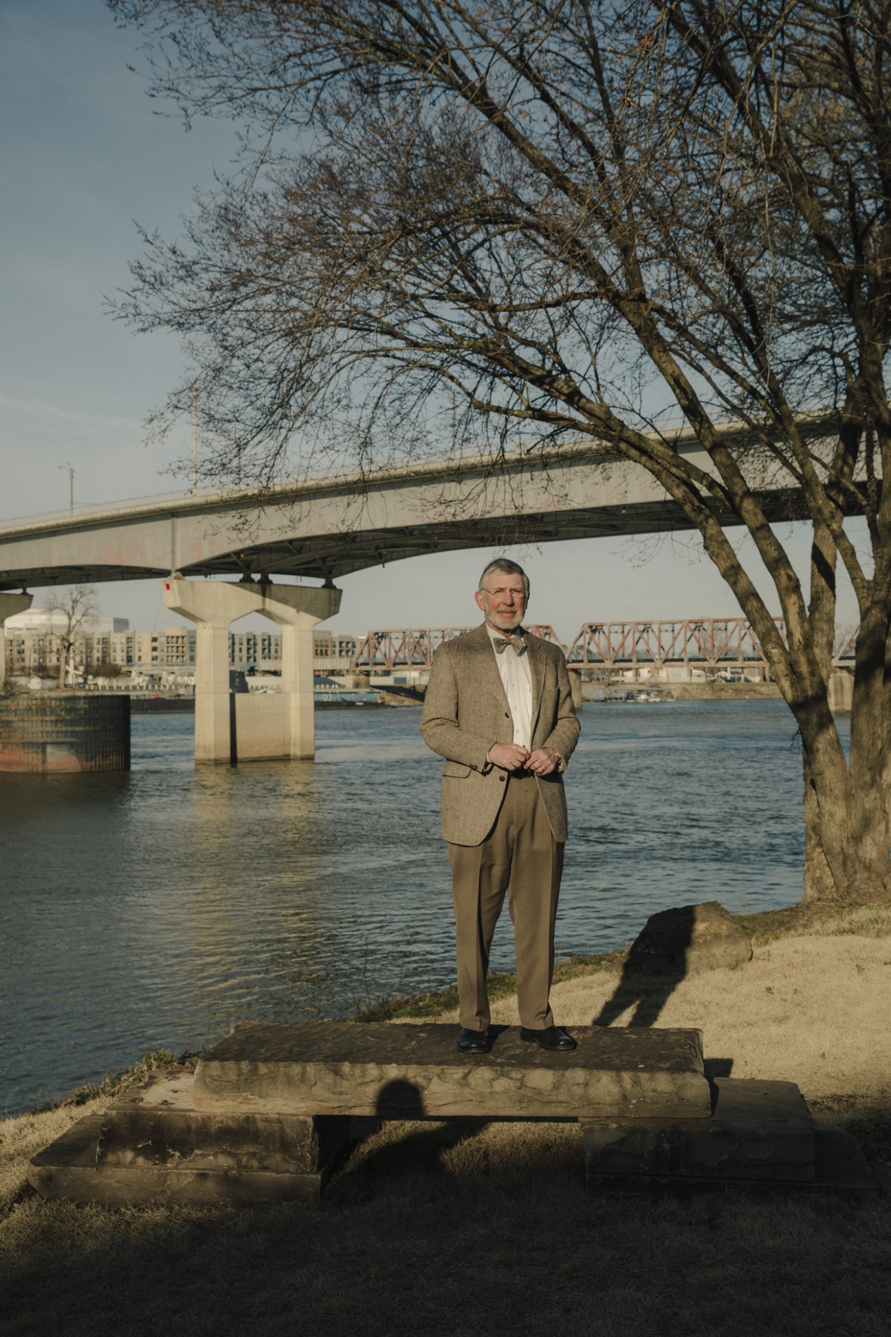 Dean Kumpuris stands by the Arkansas River near River Market in Little Rock, with a bridge visible in the background.