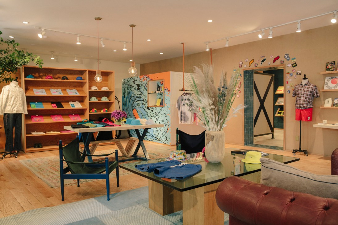 Interior of Noah's Manhattan shop featuring wooden shelving, warm-toned walls, display tables with clothing, and casual seating areas.