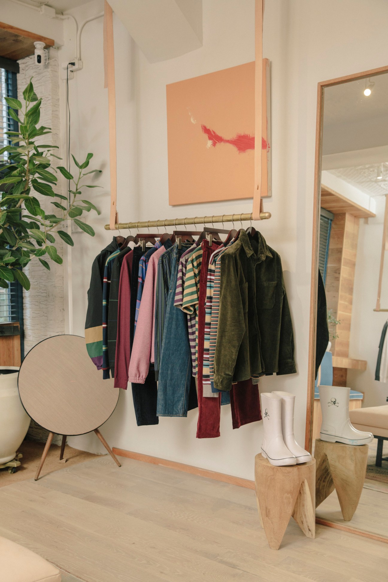 Noah retail shop interior displaying colorful clothing on a brass rail with white rubber boots and wooden display elements.