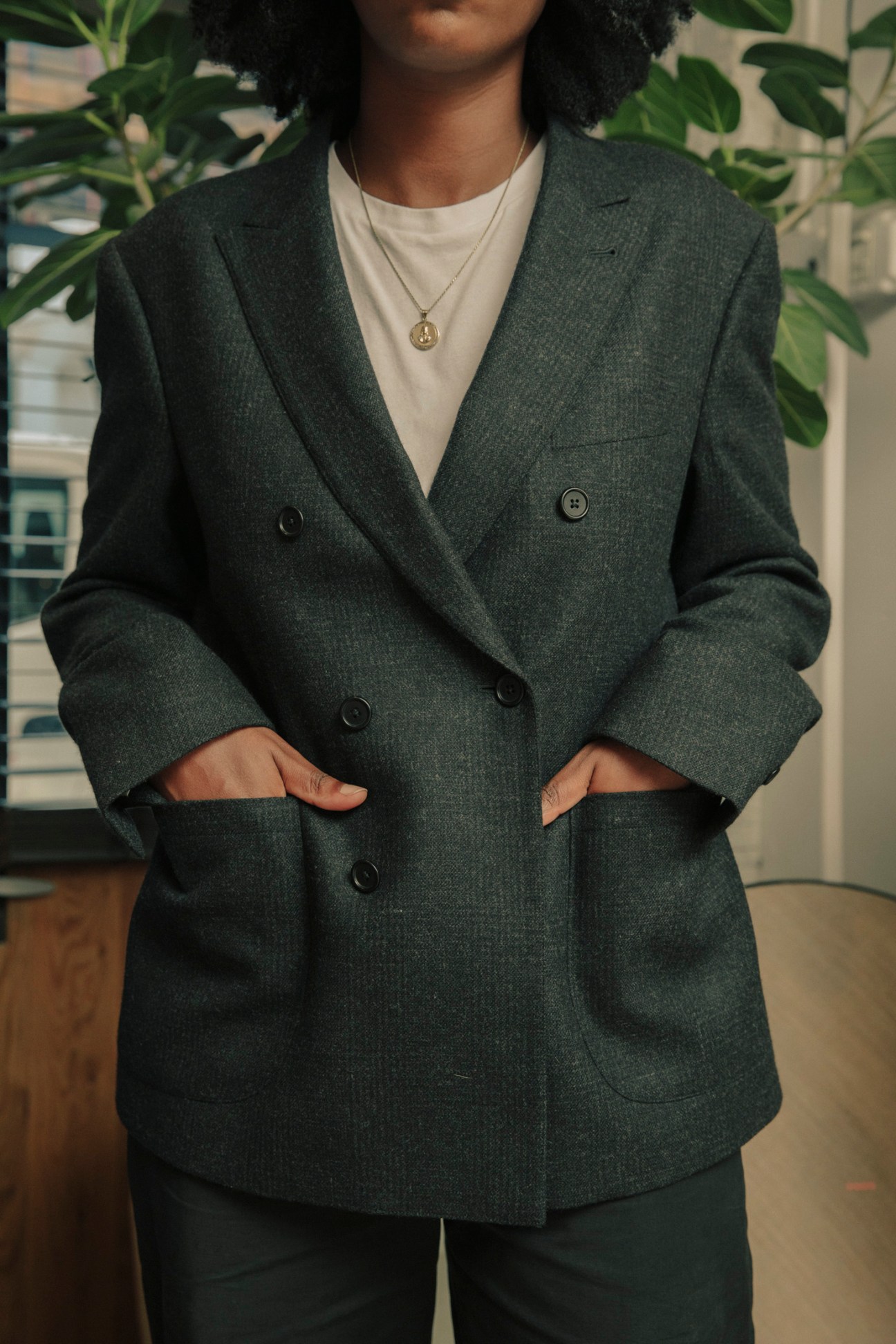 Person wearing a charcoal wool-and-cashmere double-breasted sport coat with white t-shirt underneath and gold pendant necklace.