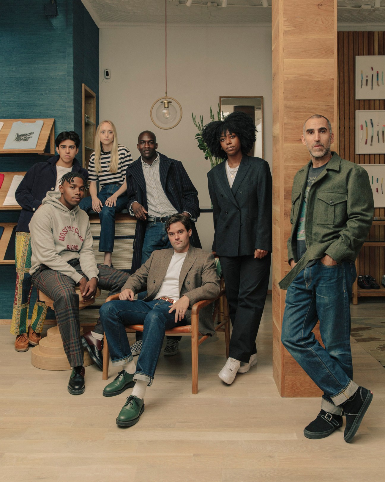 Seven people posing in Noah's Manhattan shop, styled in contemporary casual and tailored clothing among wooden fixtures and shelving.