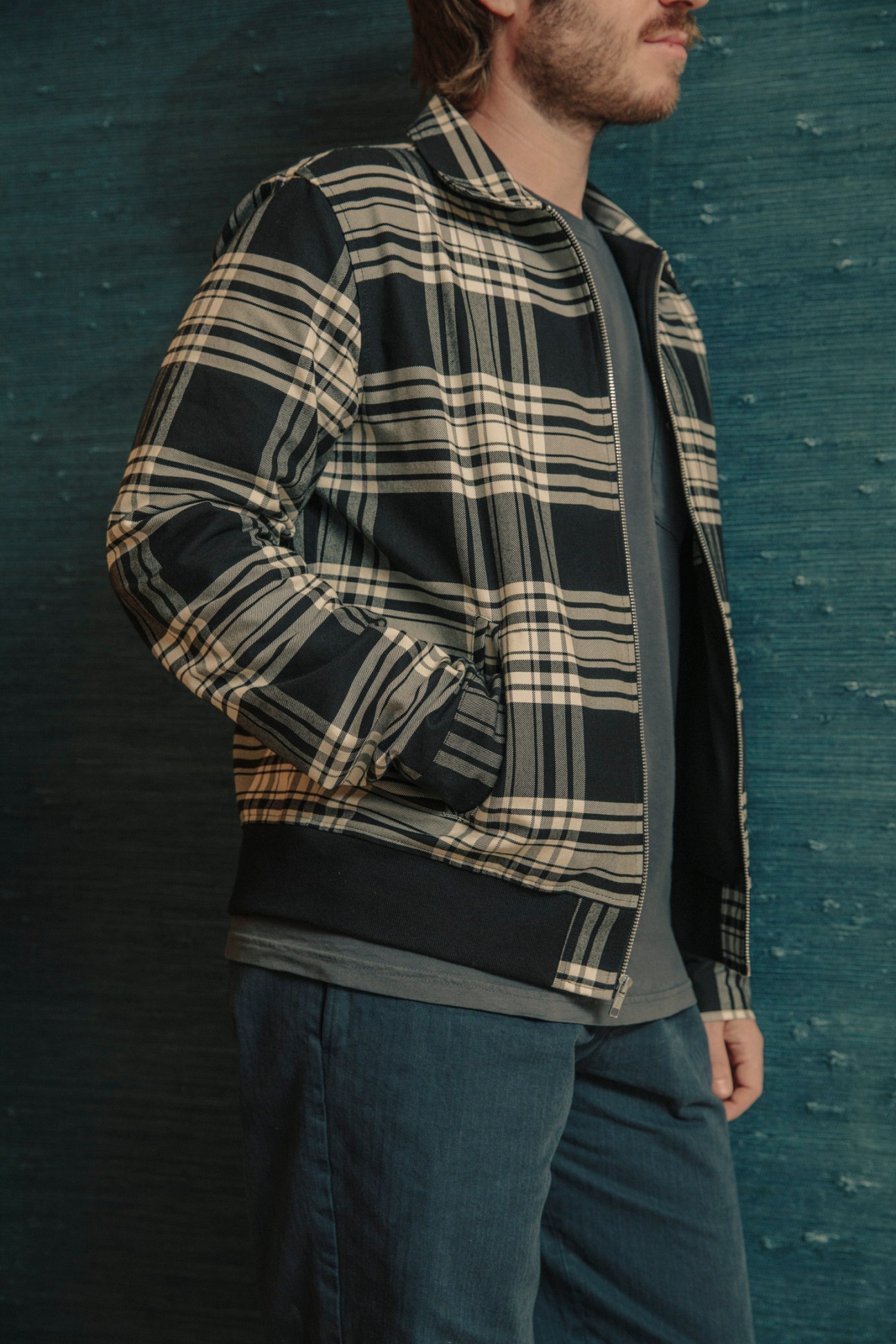 Man wearing a tartan plaid bomber jacket in black and cream utility twill with denim jeans.