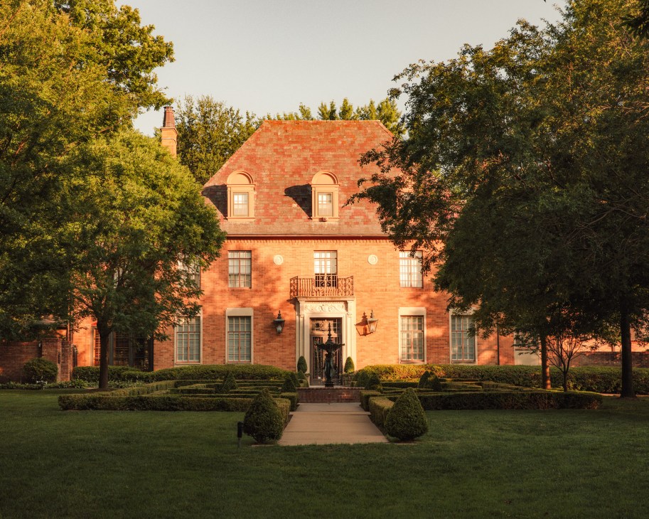 A grand brick residential home with mansard roof and manicured hedges in south Tulsa.