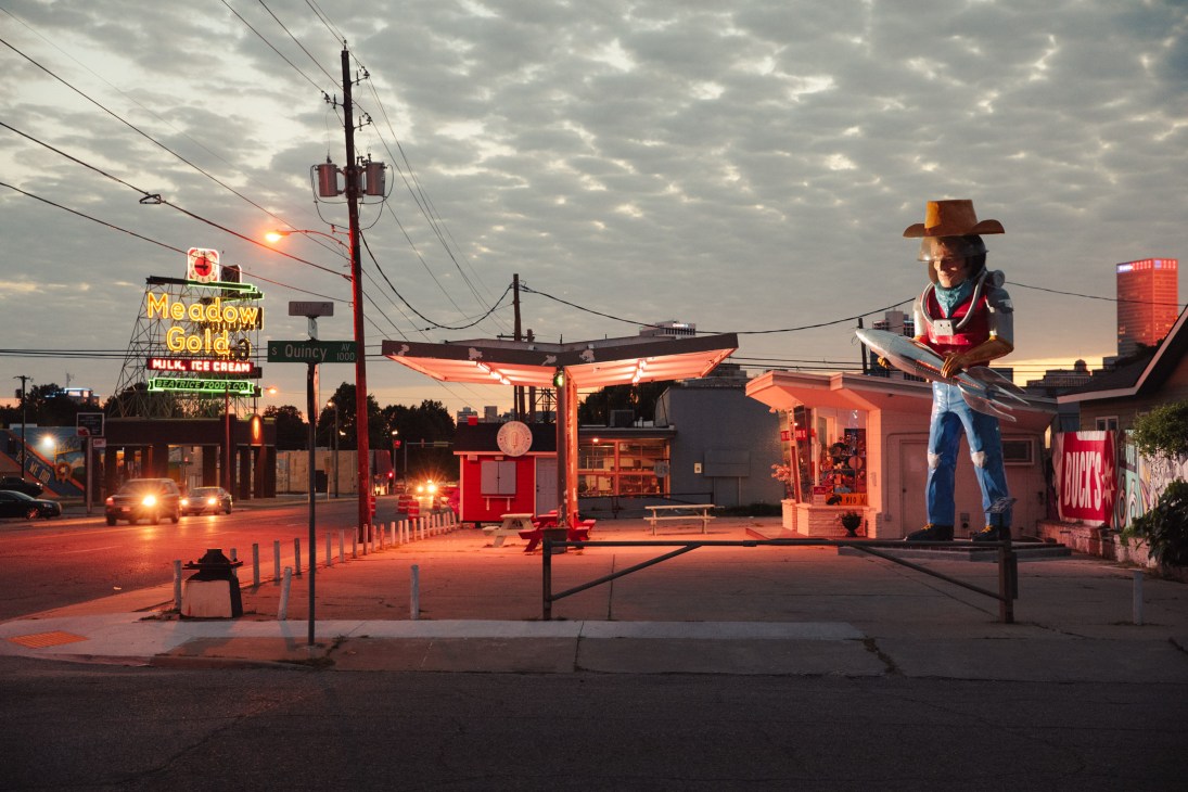 Buck Atom Space Cowboy statue illuminated at dusk on Route 66 with vintage neon signs and buildings.