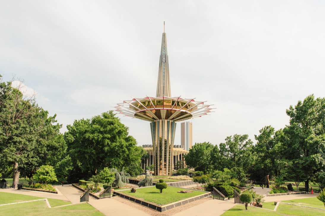 Prayer Tower at Oral Roberts University, a tall modern spire with a golden disc-shaped structure at its base surrounded by green trees.