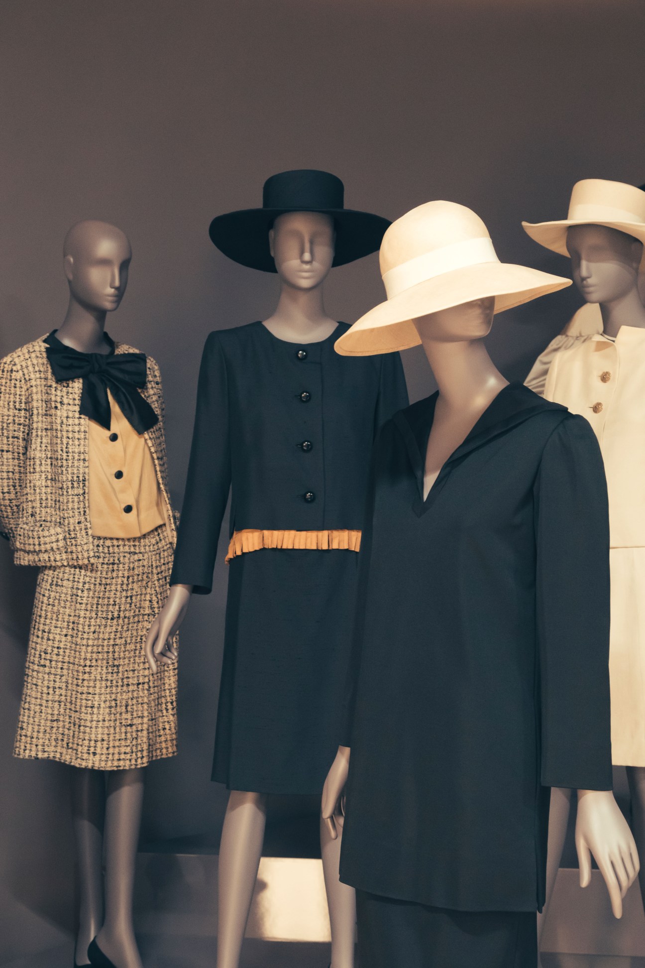 Four mannequins display Yves Saint Laurent classic designs including a tweed suit, black dress with orange trim, and elegant hats.