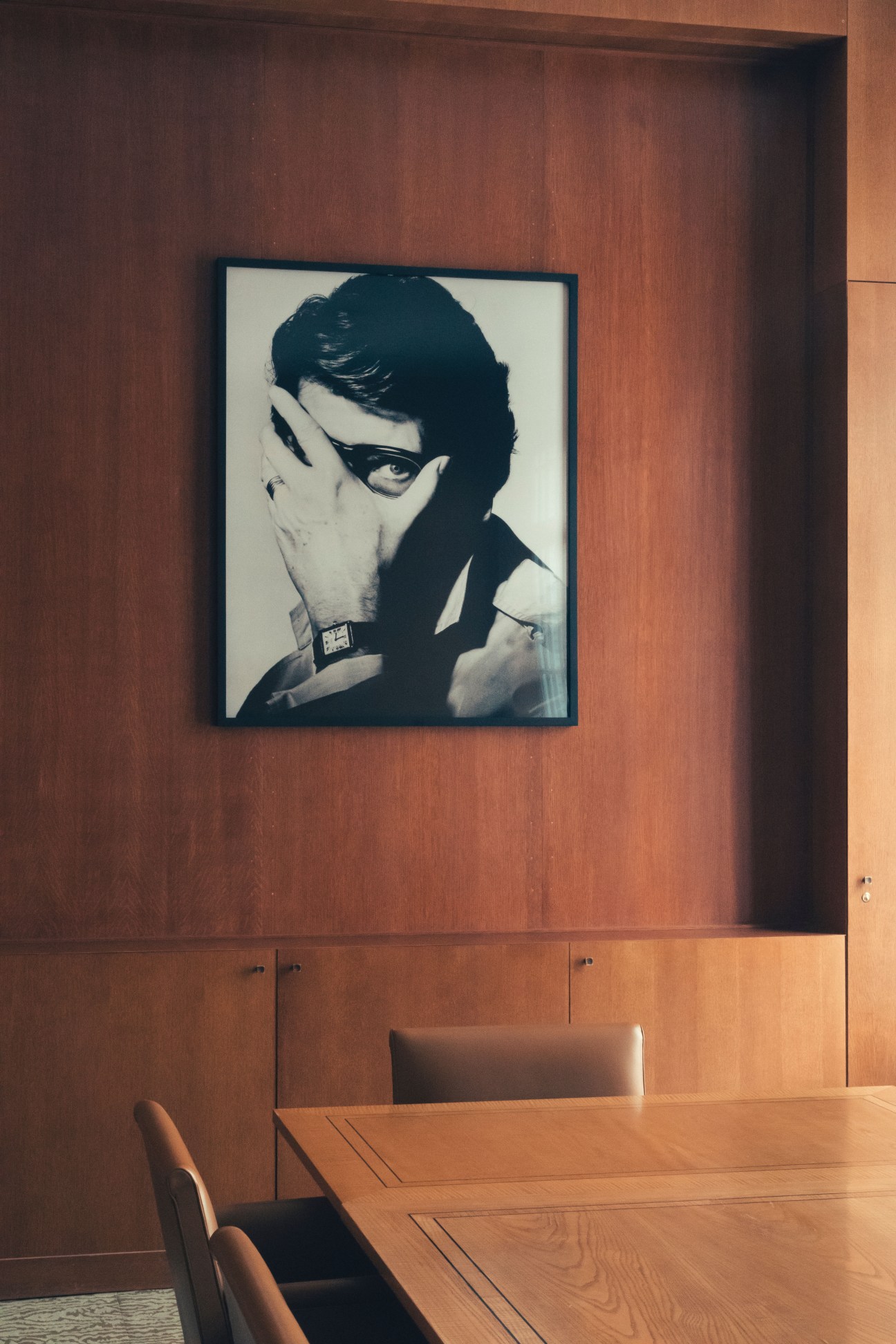 Oak-paneled boardroom with a framed black and white portrait of Yves Saint Laurent wearing sunglasses and a collared shirt.
