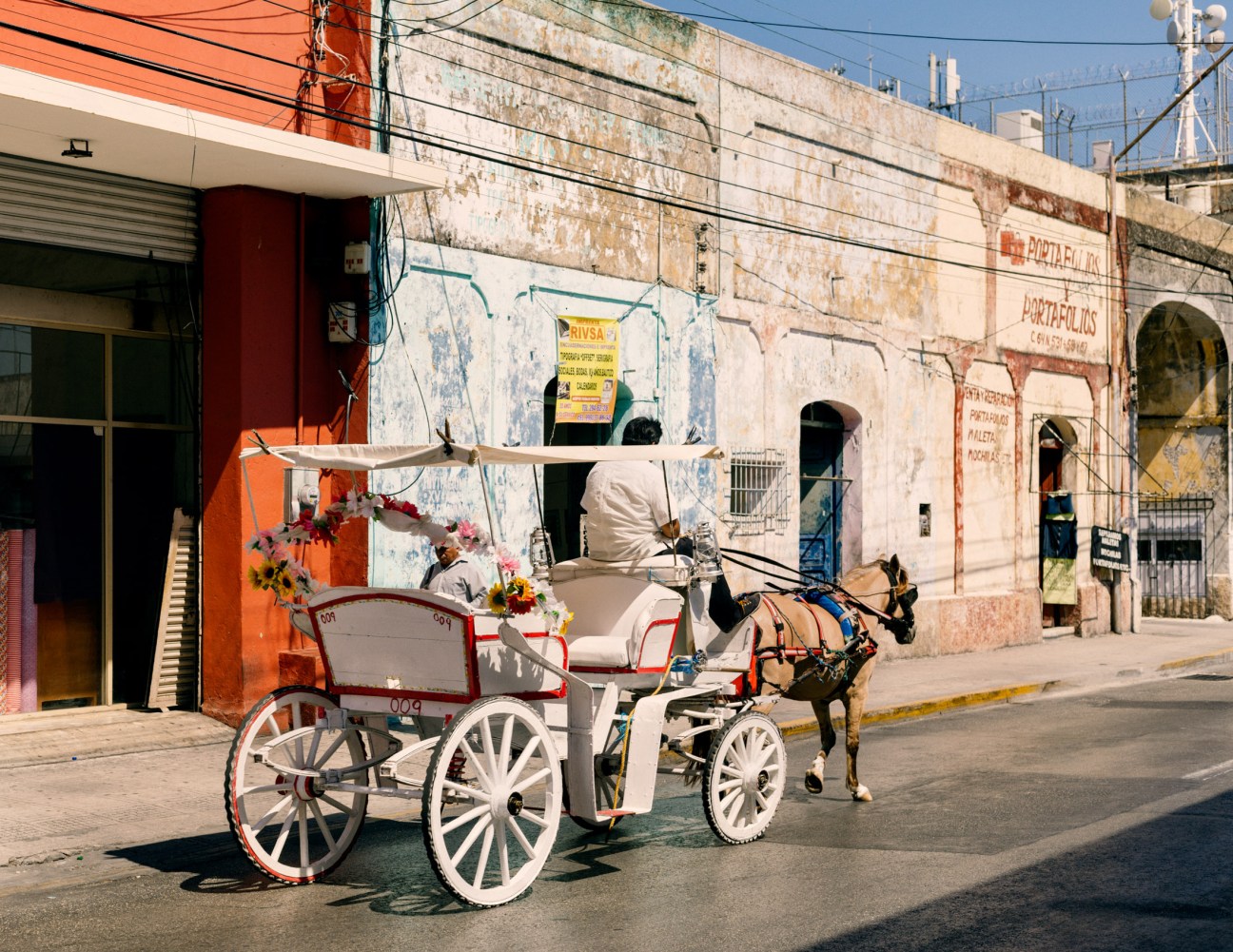 A horse-drawn carriage with white wheels and red trim on a street in Mérida's colonial center.