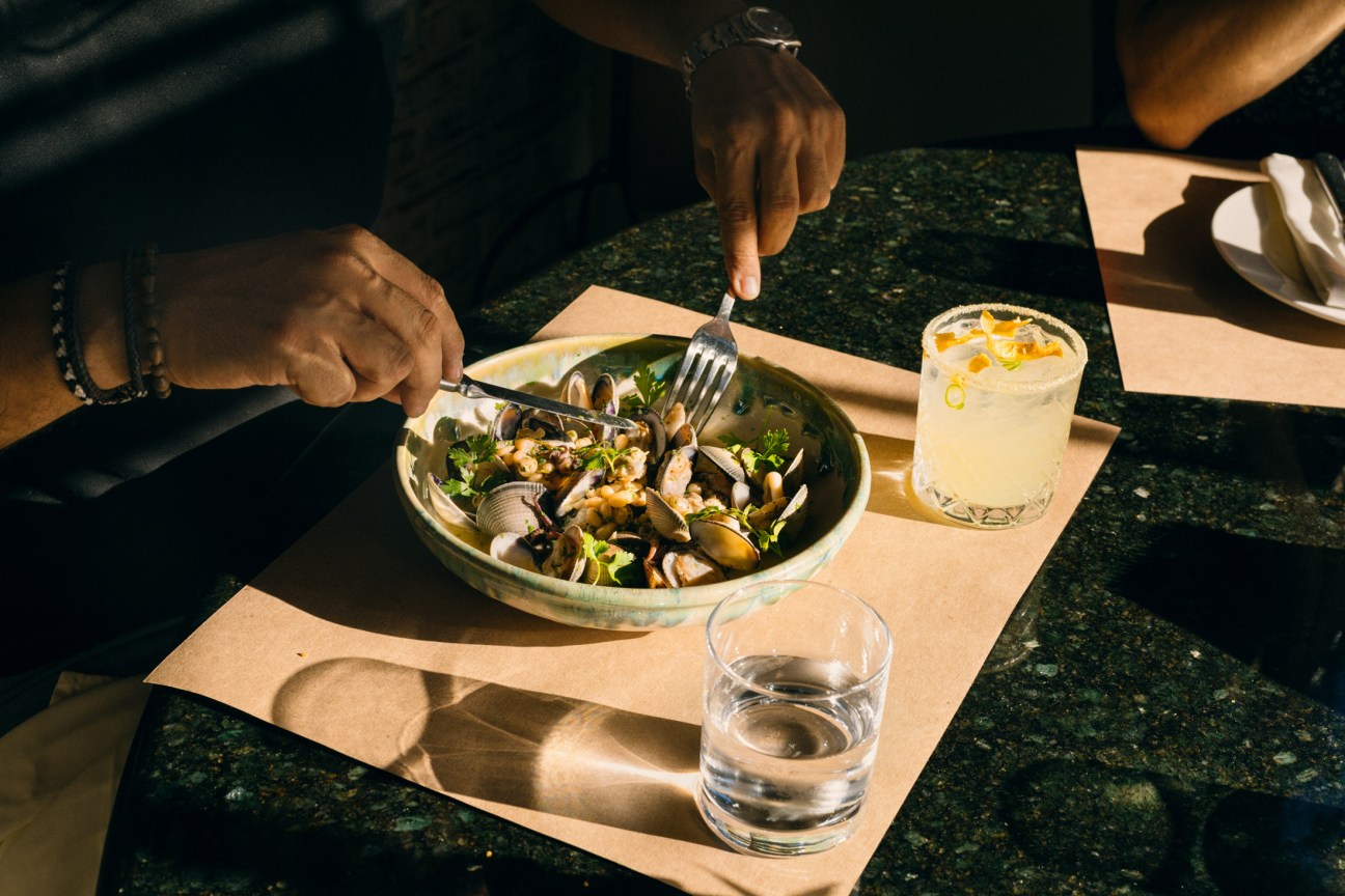 Person eating clams from a white ceramic bowl at Italian restaurant Oliva in Mérida.