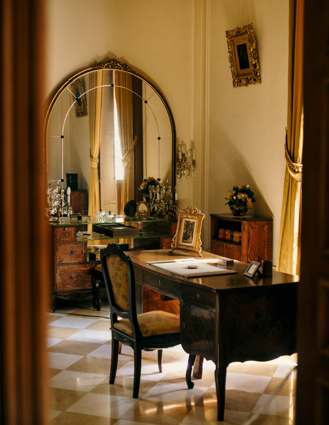Ornate vanity with large arched mirror and wooden desk in elegant cream-colored room at Quinta Montes Molina museum.