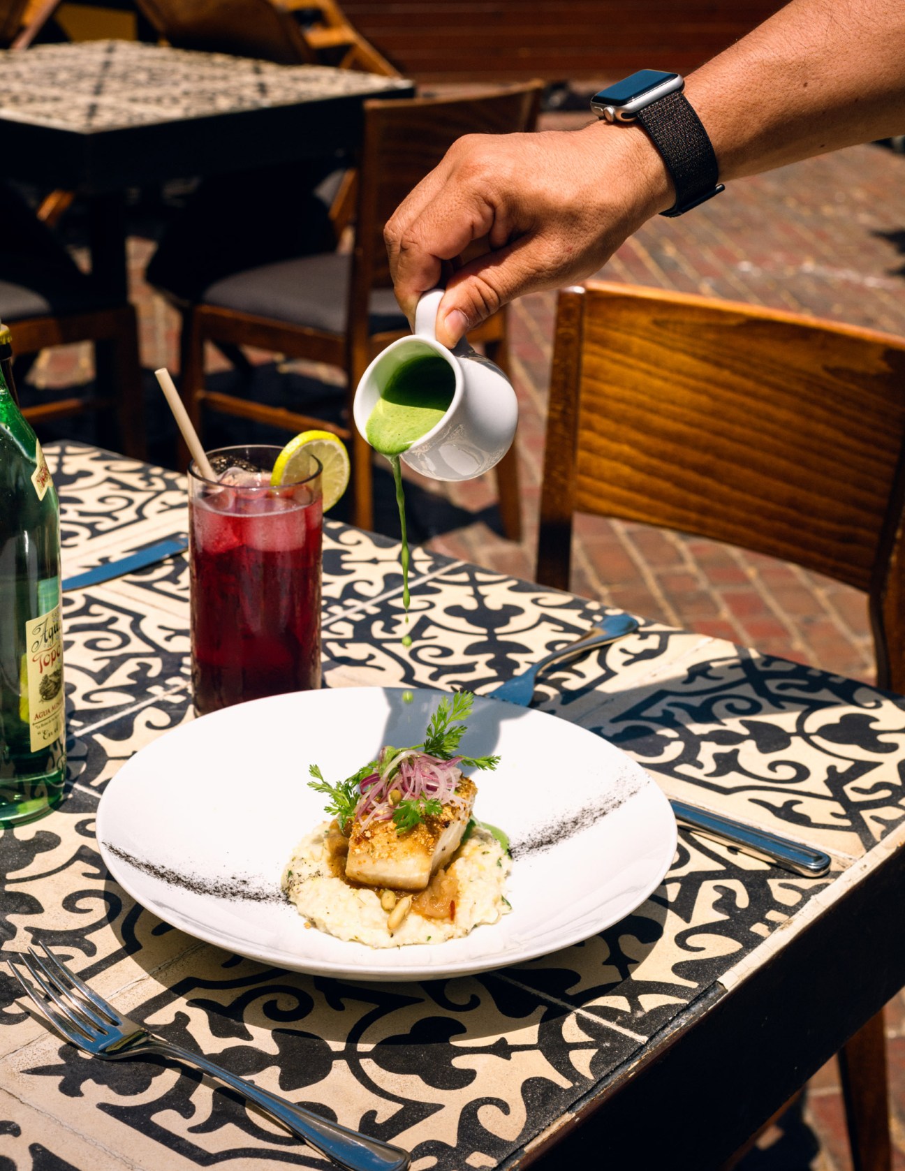 A hand pours green sauce over a plated seafood dish at Apoala restaurant in Mérida.