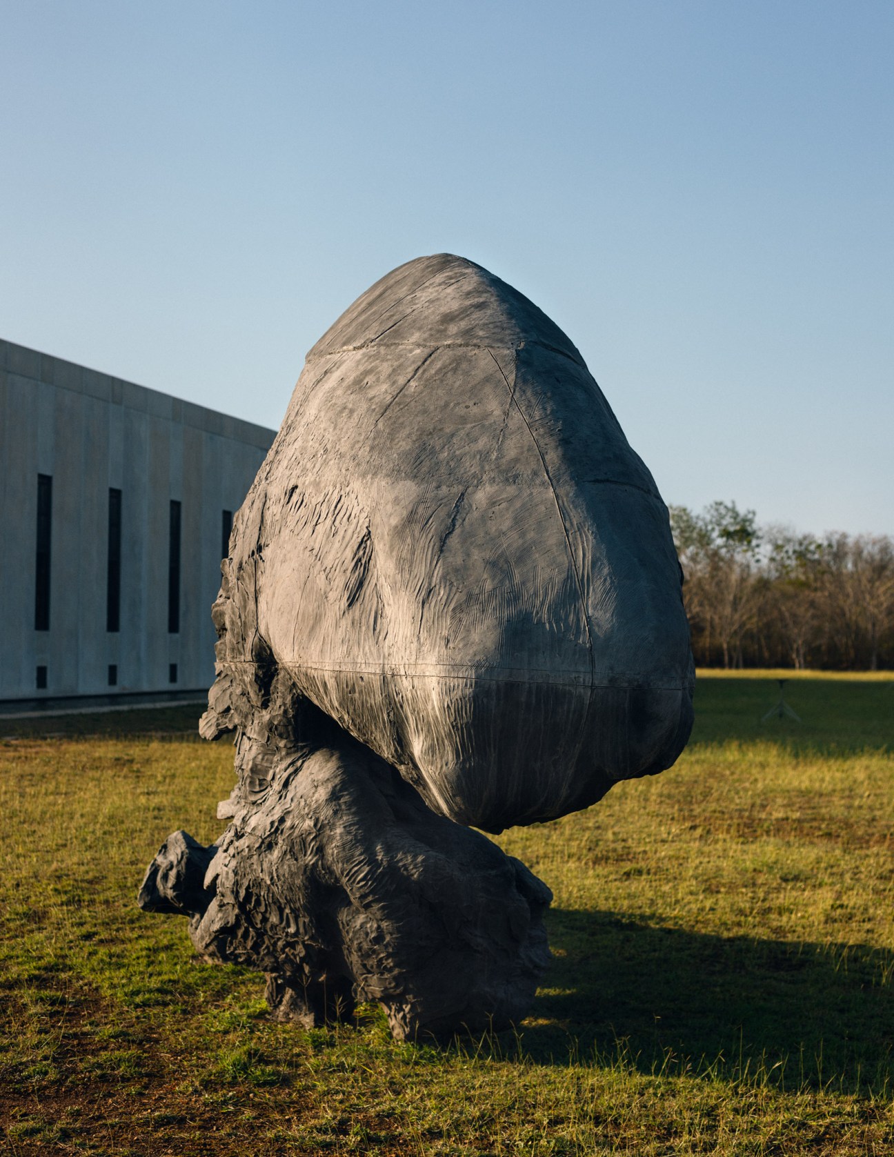 Large stone sculpture by Javier Marín depicting an abstract head at Plantel Matilde in Sac Chich, with modern building and green field in background.