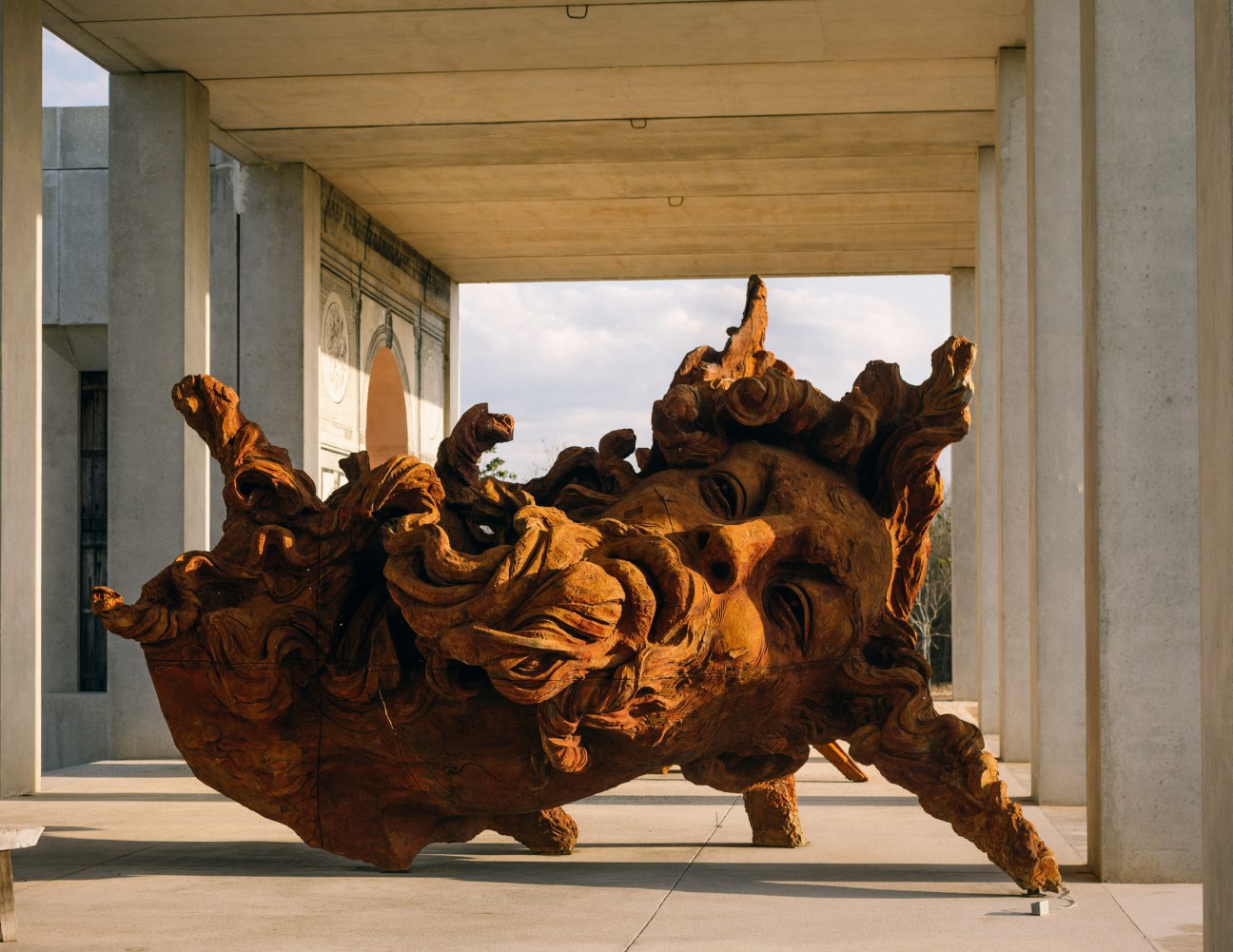 Large wooden sculpture displayed under a modern concrete structure at Plantel Matilde artist residence.